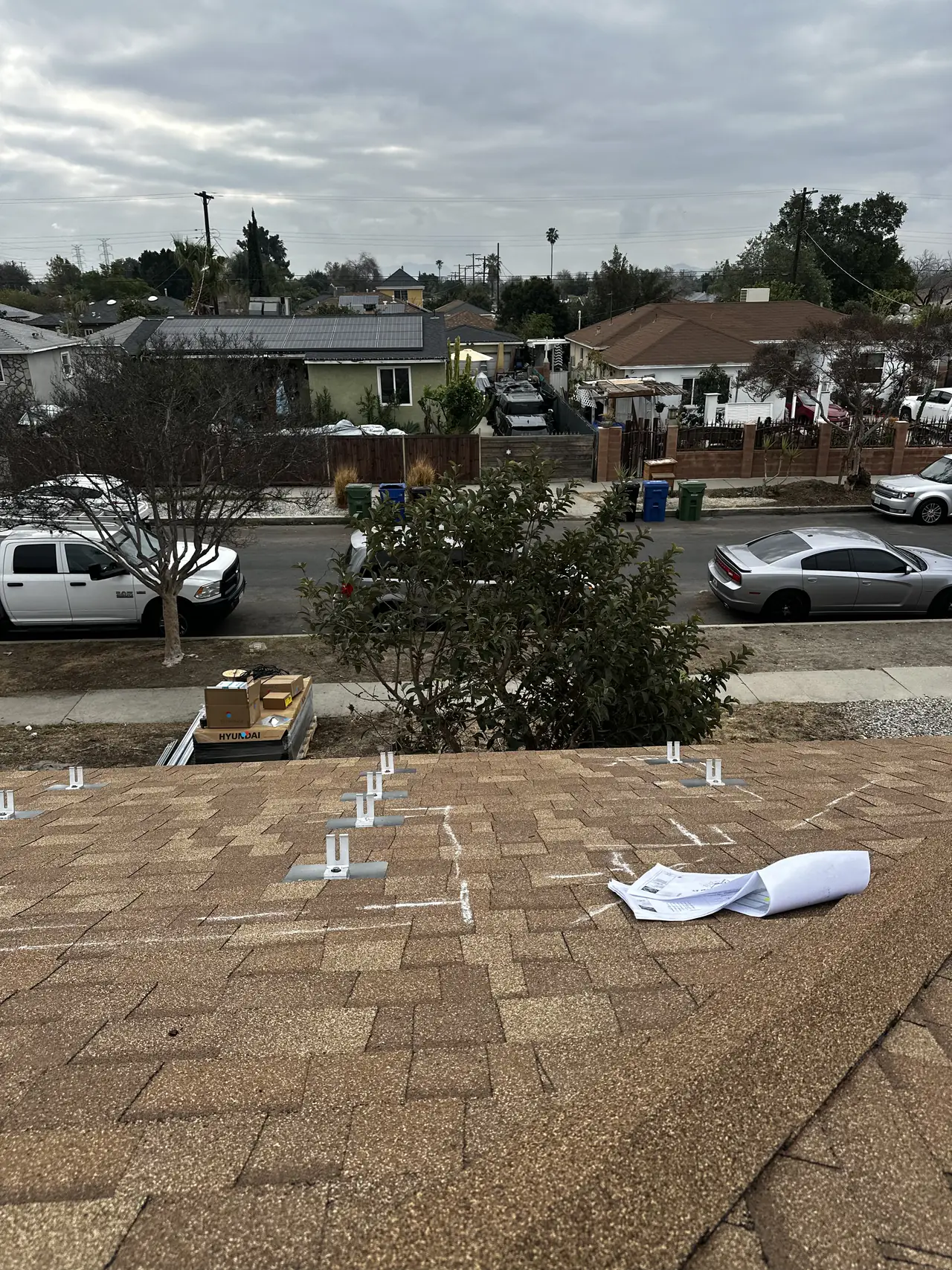 The second plane of a composition shingle roof marked with chalk layout lines and flashing plates, with the street below, Arleta, Los Angeles