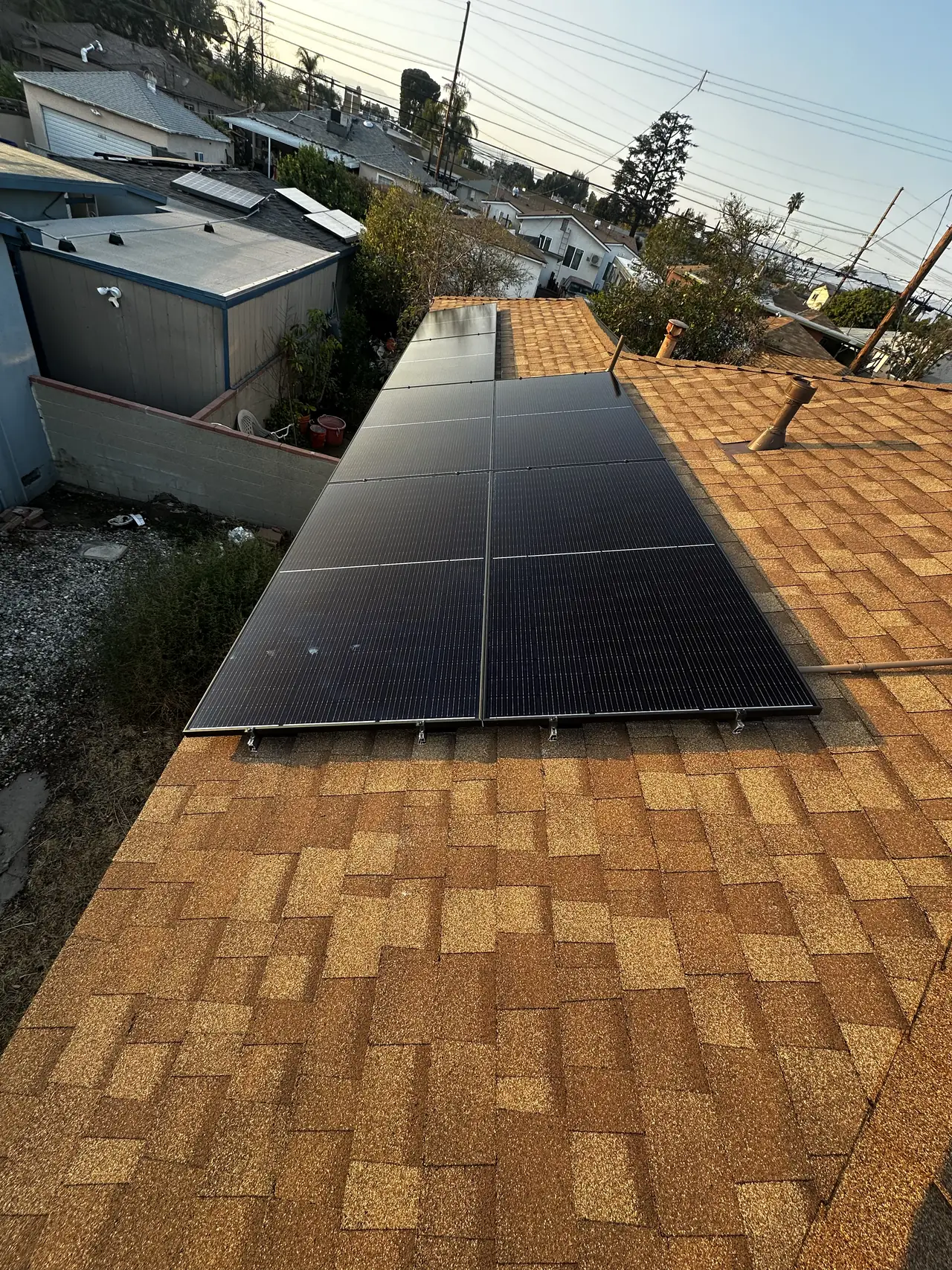 All-black solar modules installed across a composition shingle plane with neighboring rooftops beyond, Arleta, Los Angeles