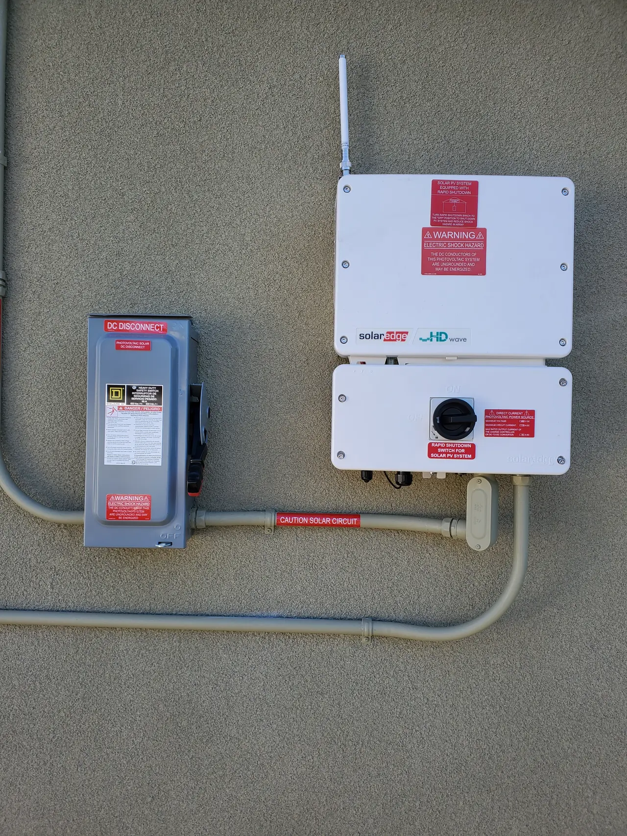 Wall-mounted string inverter with a DC safety switch and conduit on a stucco wall in Burbank