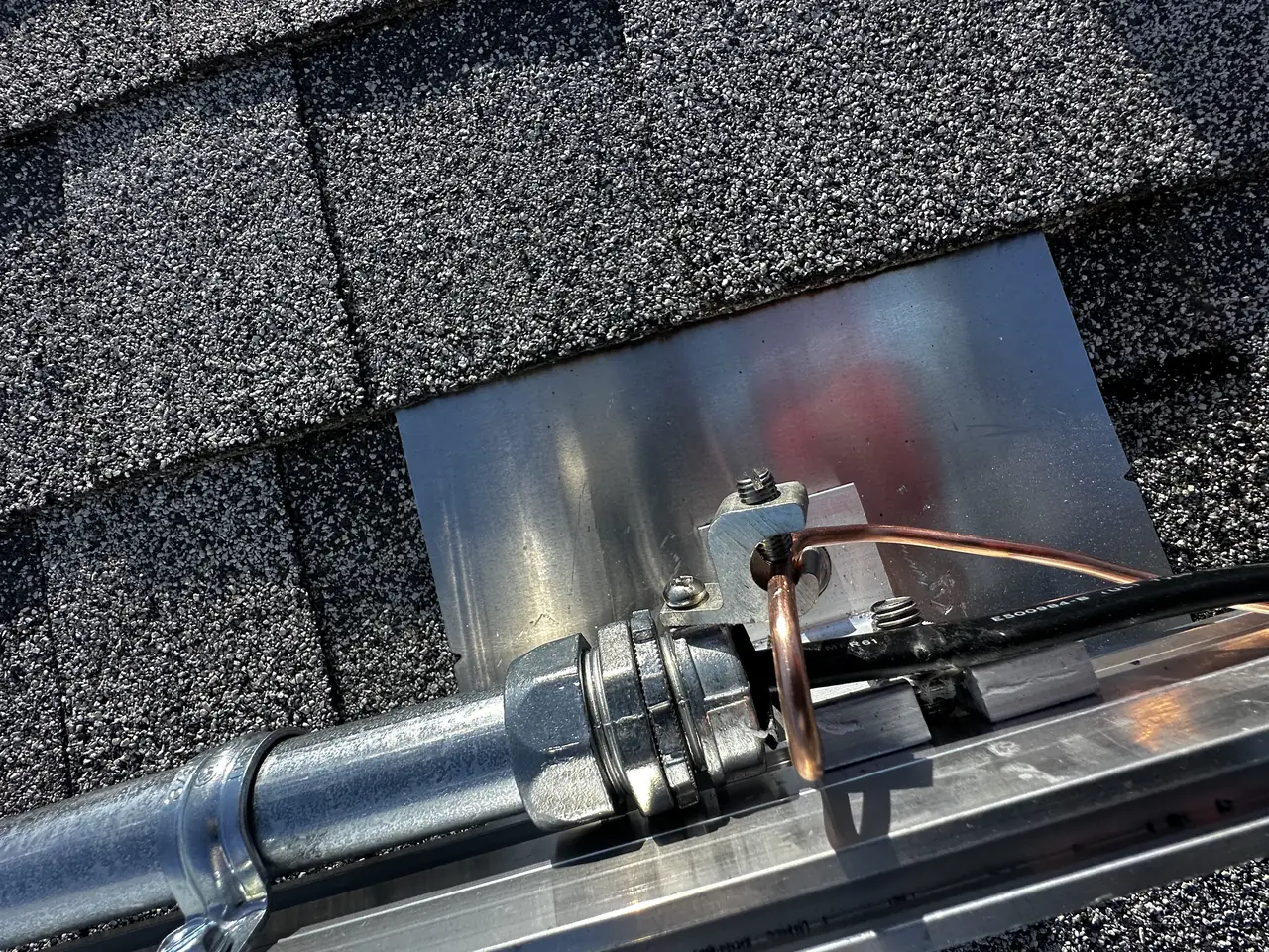 Metal flashing plate set into a shingle roof in Burbank around a conduit penetration, with sealant