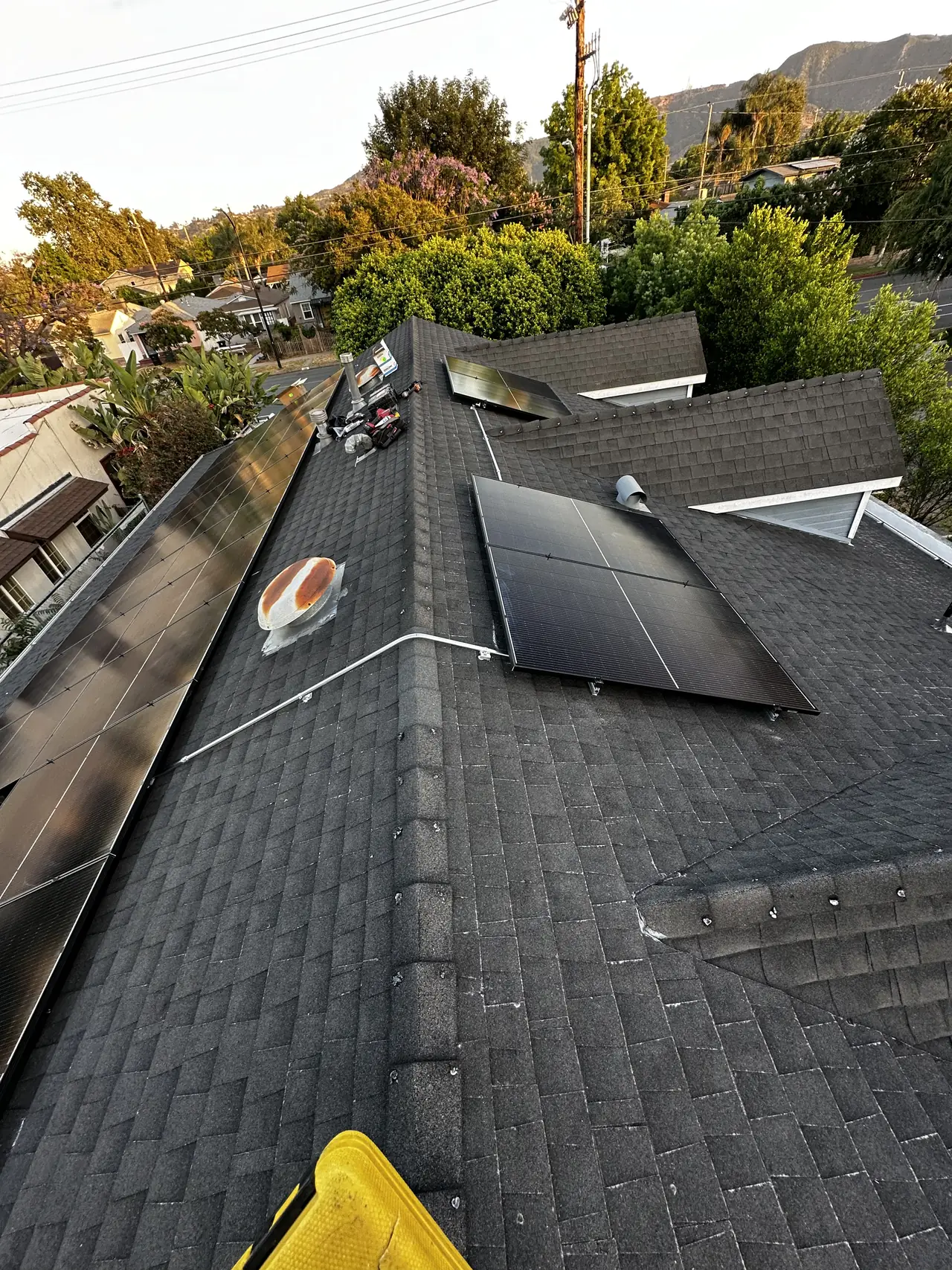 Solar modules installed across a hipped shingle roof of a Burbank house seen from the ridge