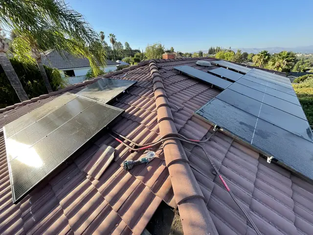 Black solar modules on both sides of a red S-tile ridge under a clear sky, Calabasas