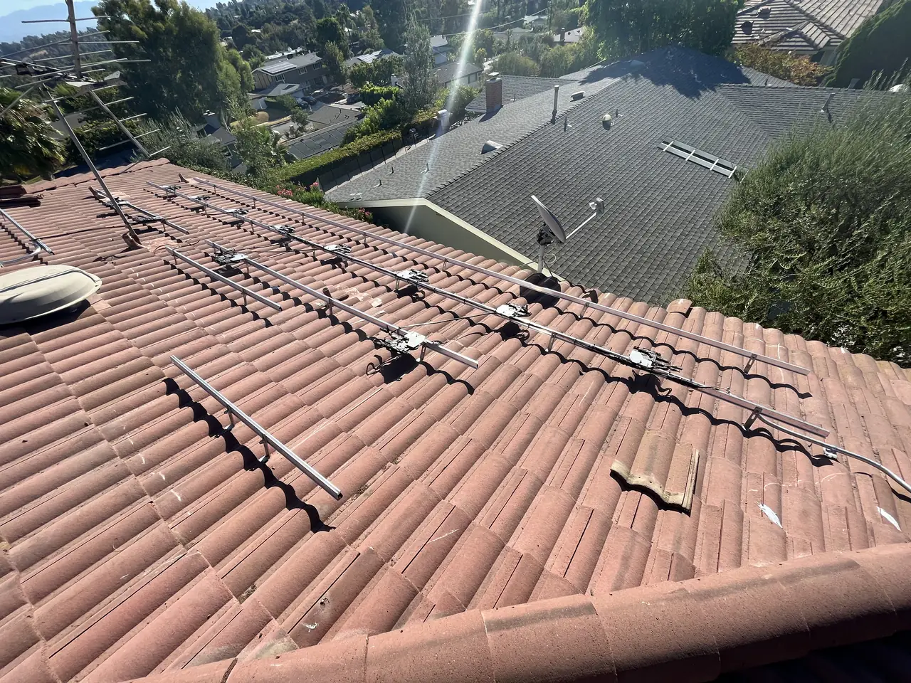 Aluminum rails with microinverters fixed across a red S-tile roof before the modules, neighboring roofs below, Calabasas