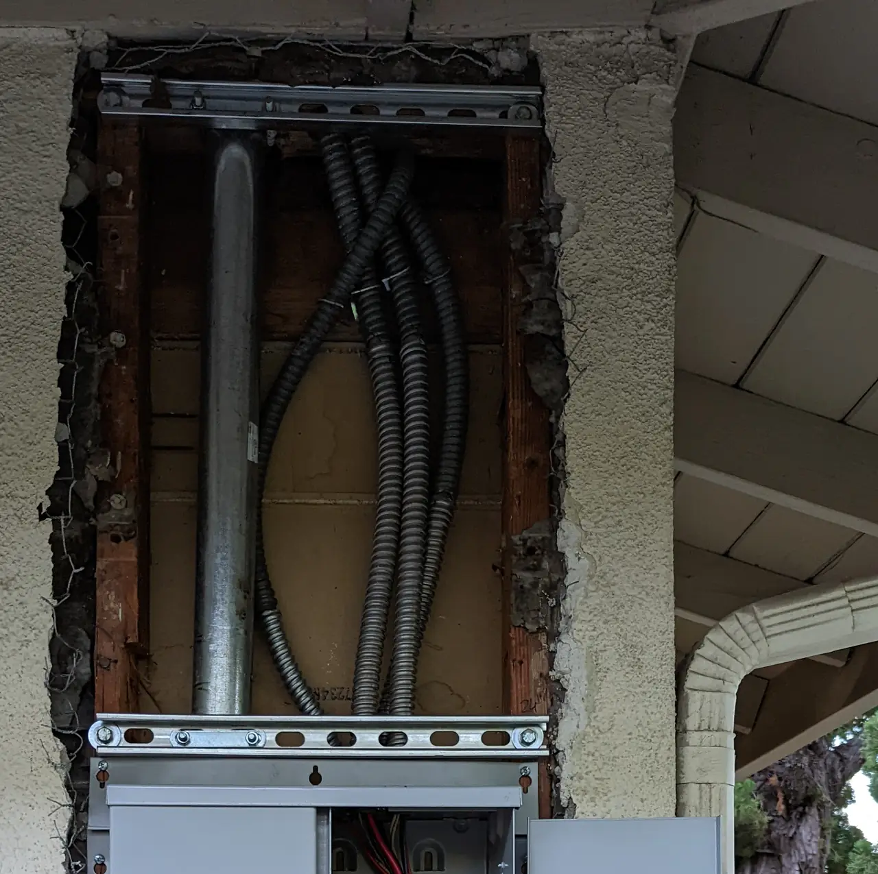 The top of a new electrical service panel set into an opening cut in a stucco wall, with conduit running up, Calabasas