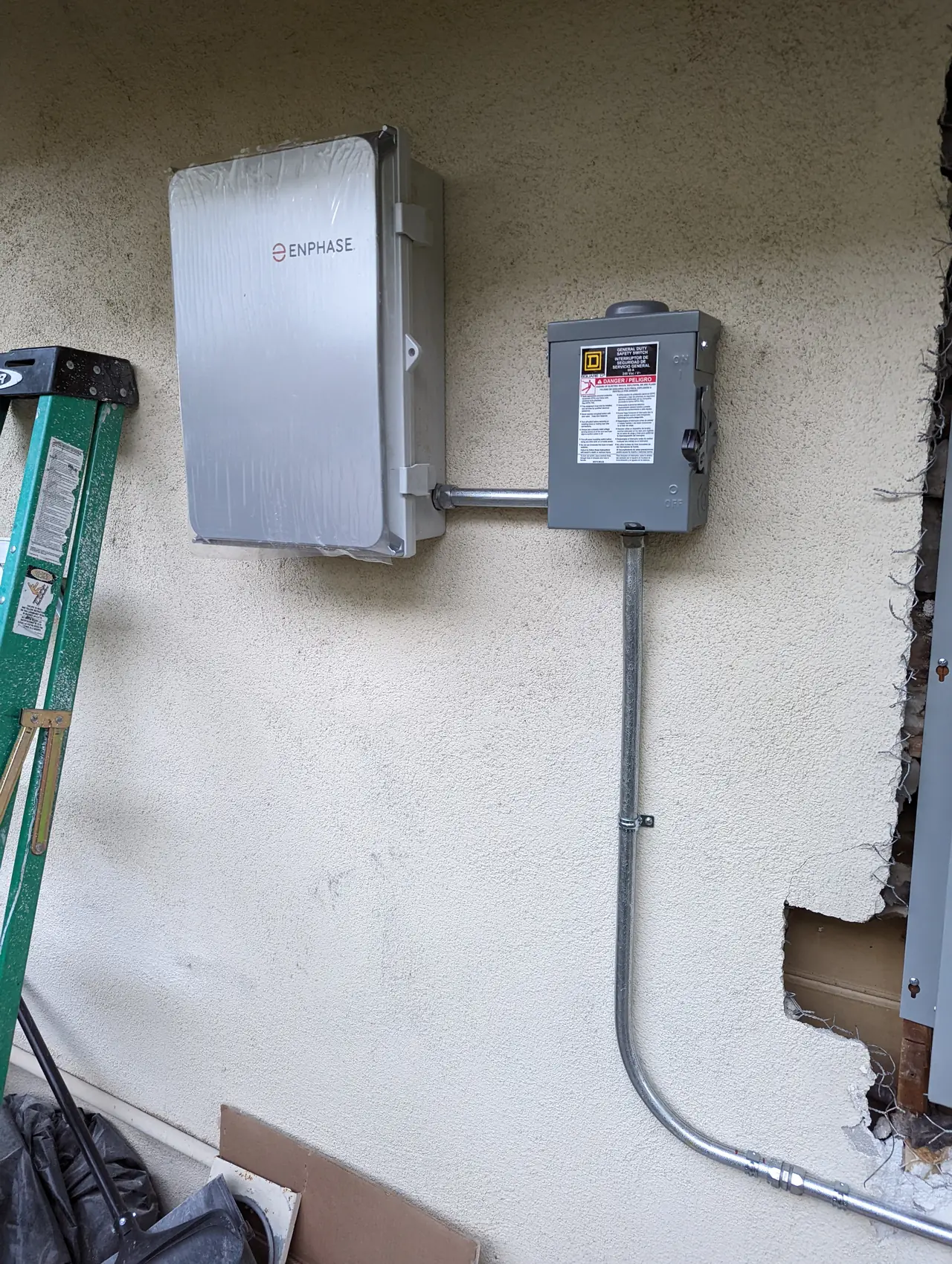 An Enphase combiner box and an AC disconnect on a stucco wall with conduit running down, Calabasas