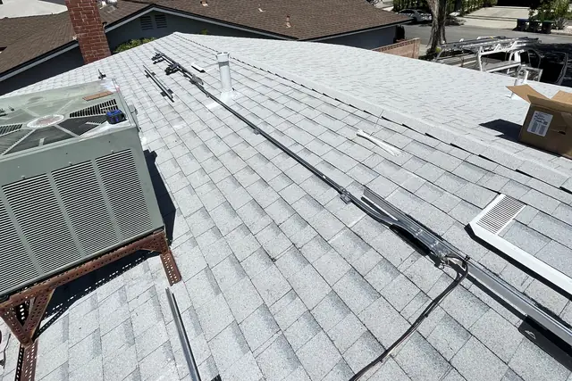 An air-conditioning condenser on a new white shingle roof beside rails and microinverters, before the modules, Calabasas