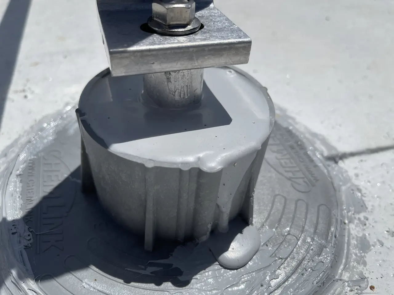 A solar standoff post set in a round curb filled with gray sealant on a white flat roof, Calabasas