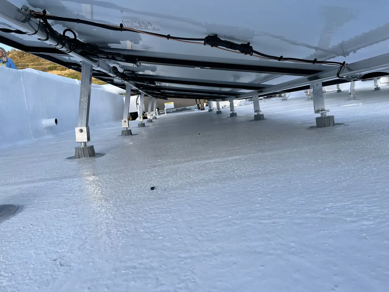 The underside of a solar array on aluminum legs over a white coated flat roof, Calabasas