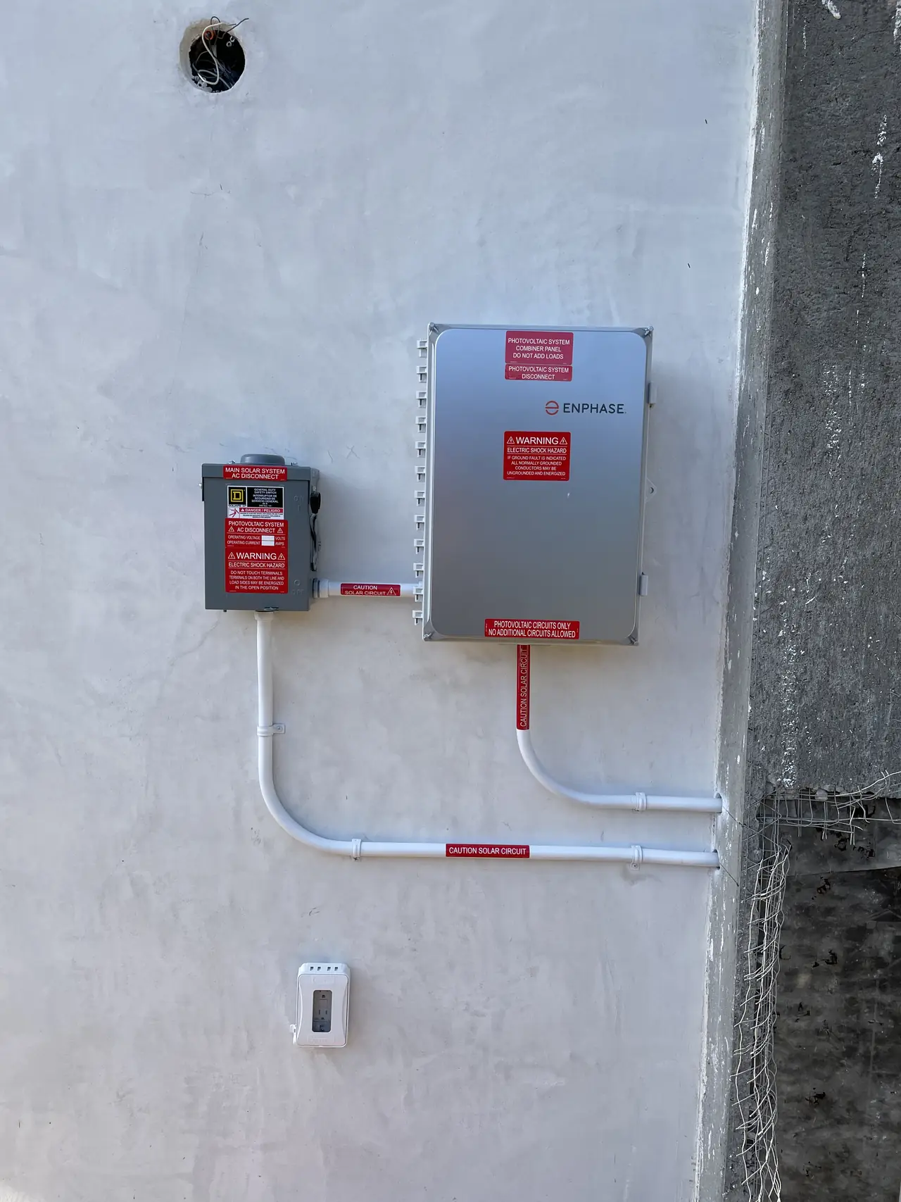 An Enphase combiner and an AC disconnect on the white wall of a new house, Calabasas