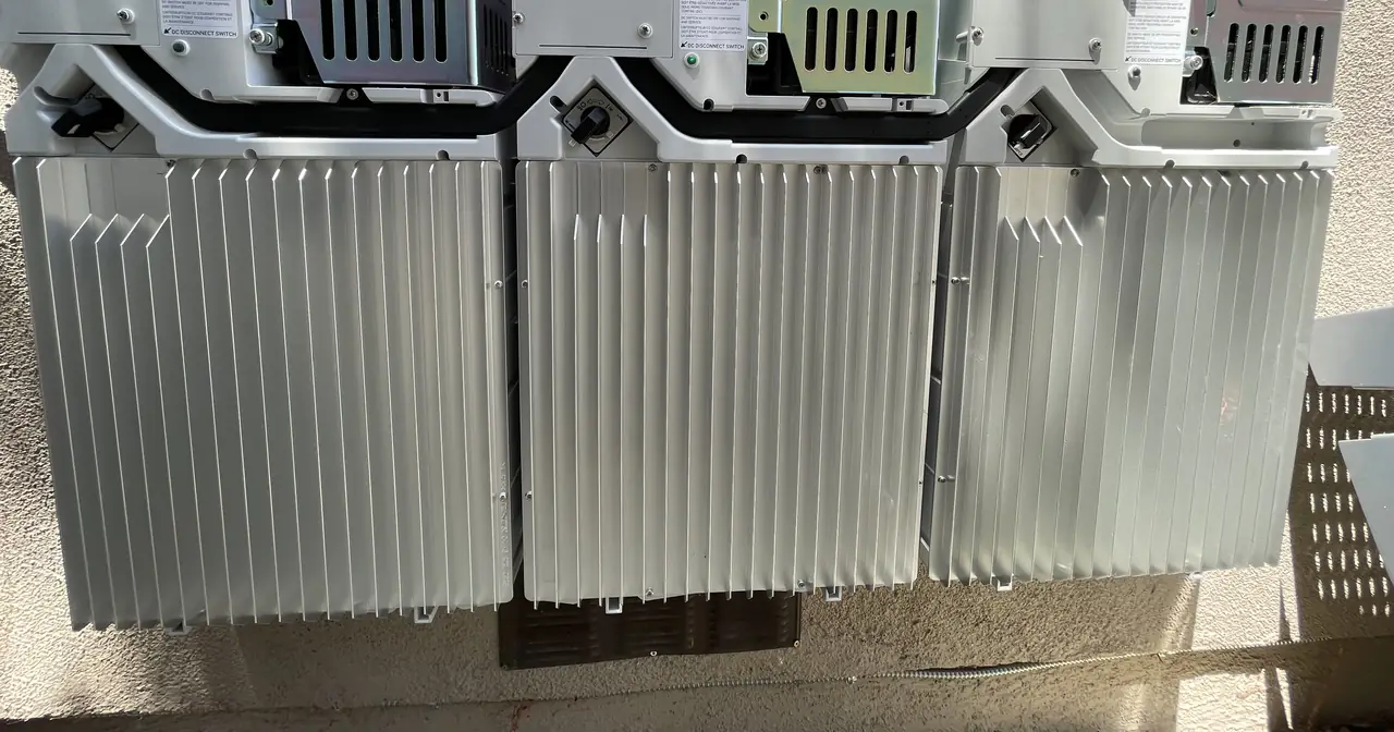 Three Enphase battery units mounted on a stucco wall with finned heat sinks facing out, Encino