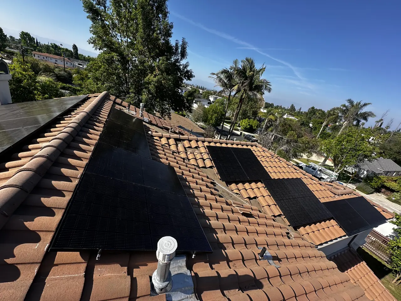 Black solar modules on both slopes of a concrete tile roof in Encino, running along the ridge with hills beyond