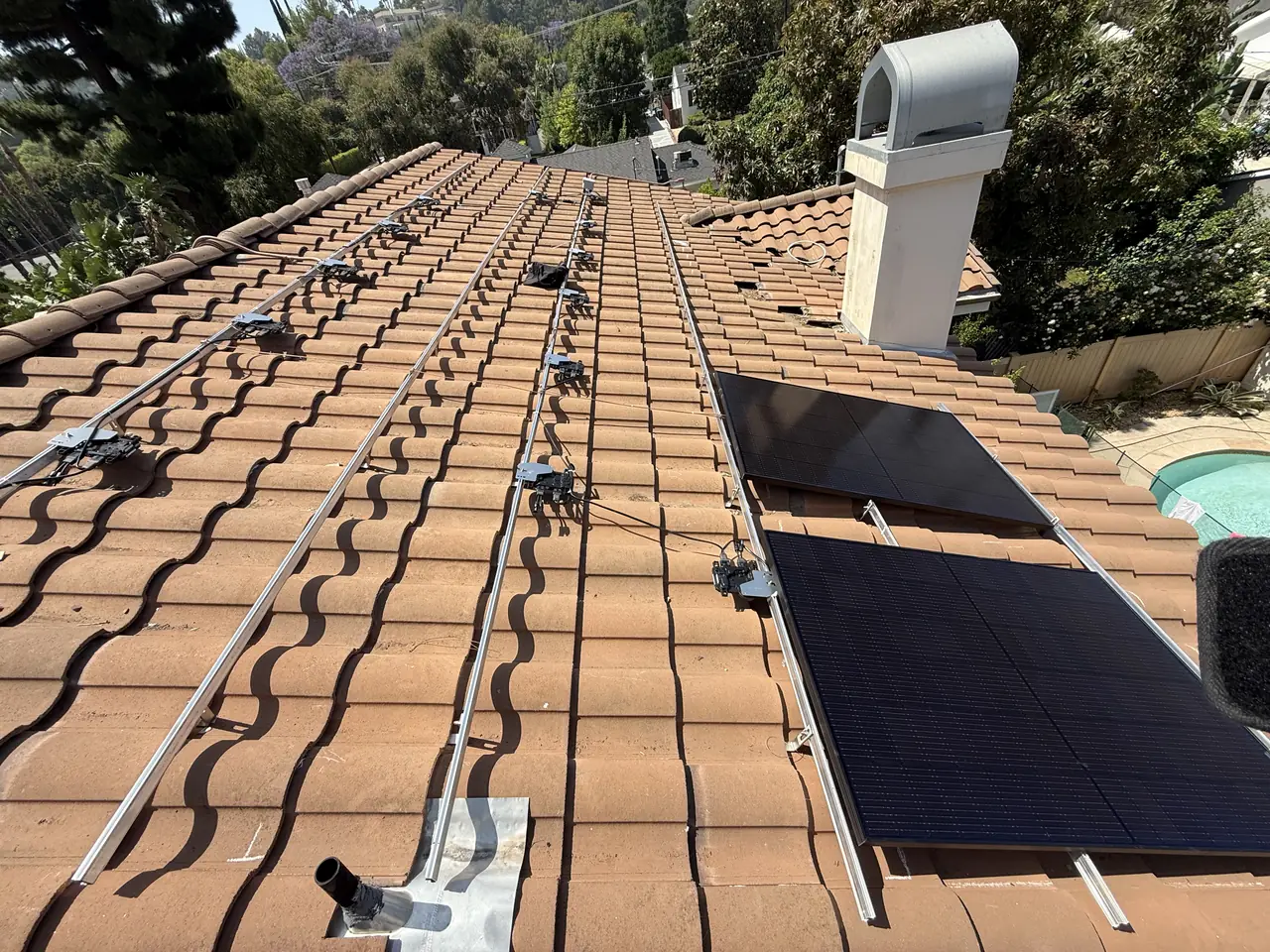 First modules being set on the rails of a tile roof, with flashing visible at a mount point, Encino