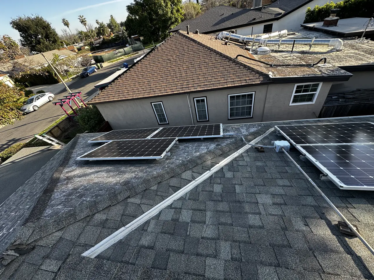 Shingle roof of a single-story Encino house with newly installed solar modules on two planes and the street beyond
