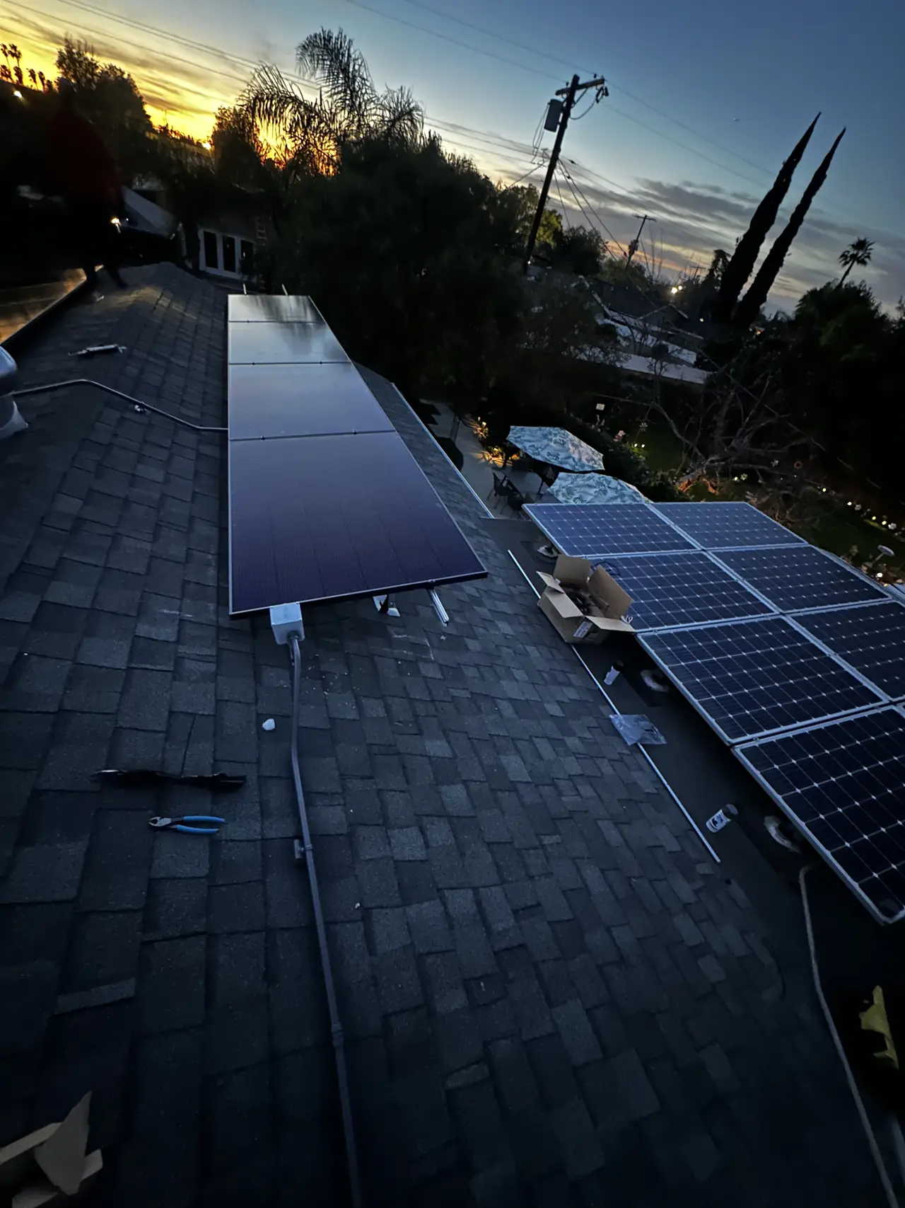 New black solar modules on a shingle roof at dusk, beside an older array with light-colored frames