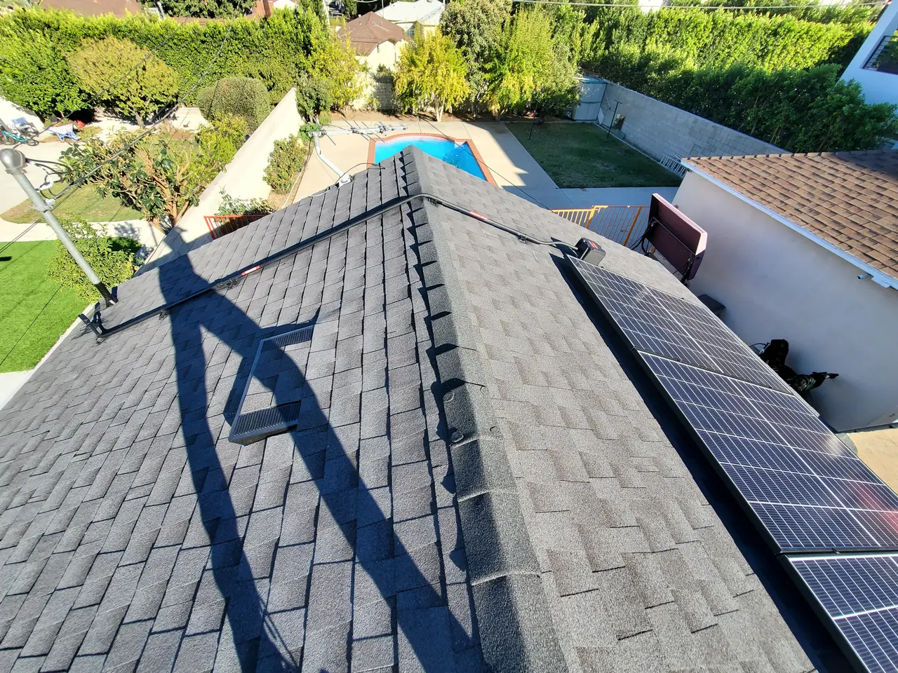 Hip roof of a single-story Encino house with new composition shingle and solar modules along one slope, a pool and yard beyond