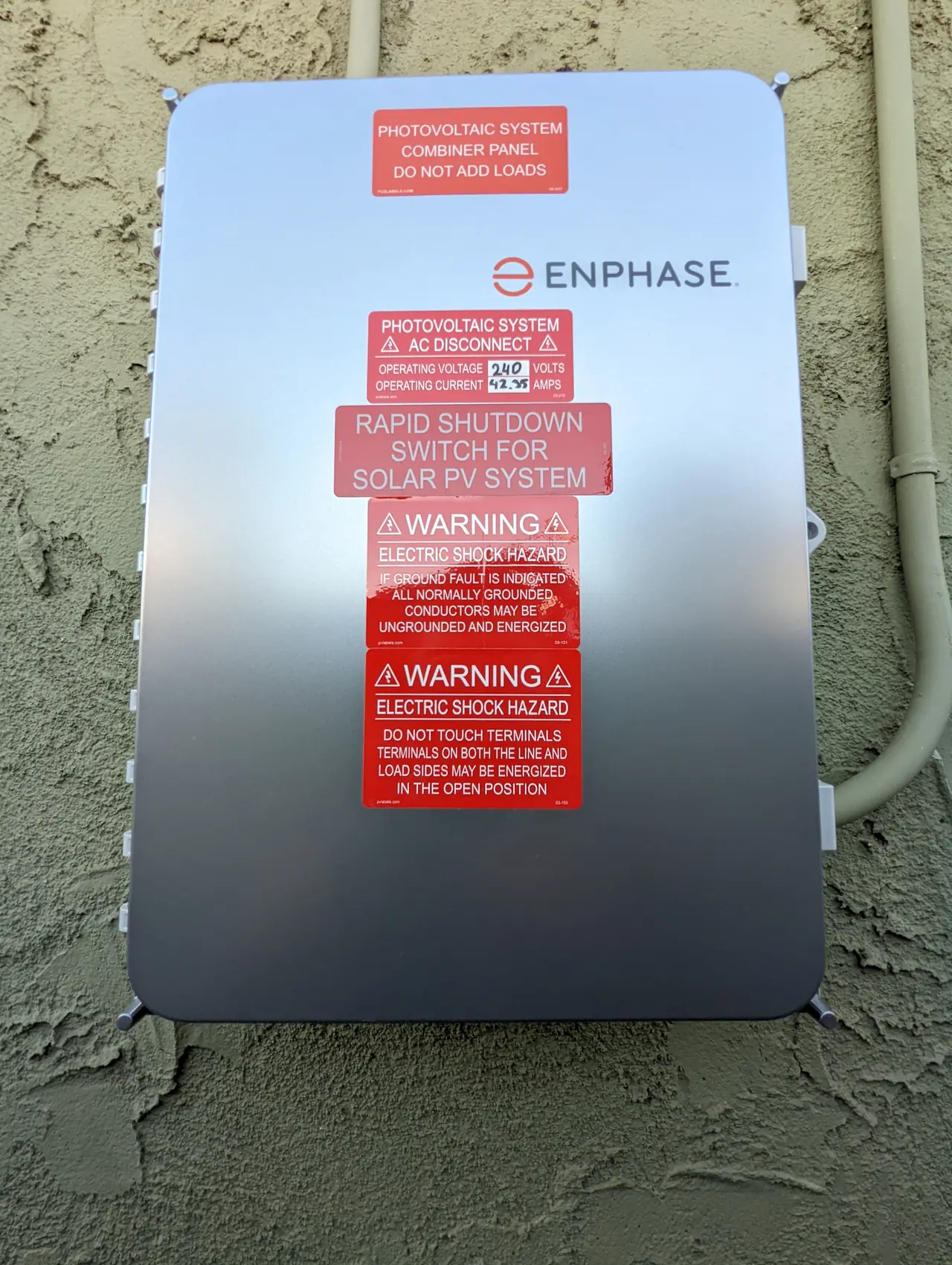 Enphase combiner panel with rapid shutdown and photovoltaic system warning labels mounted on a stucco wall
