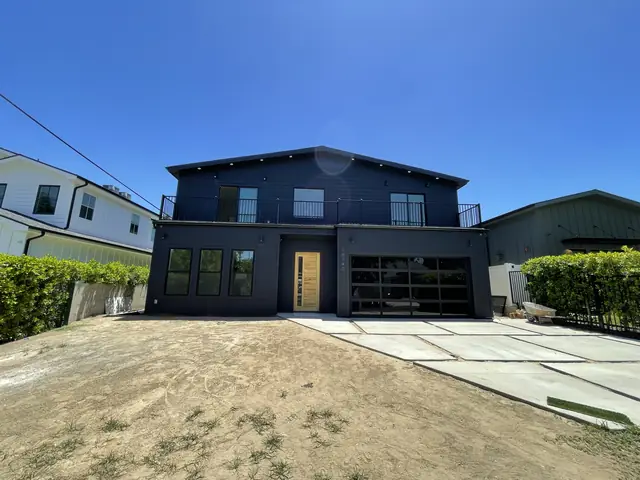 Newly finished two-story house with dark siding and an attached garage in Encino, front yard still bare earth