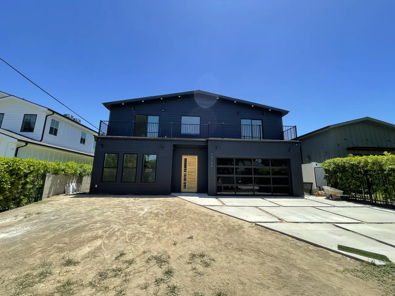 Newly finished two-story house with dark siding and an attached garage in Encino, front yard still bare earth