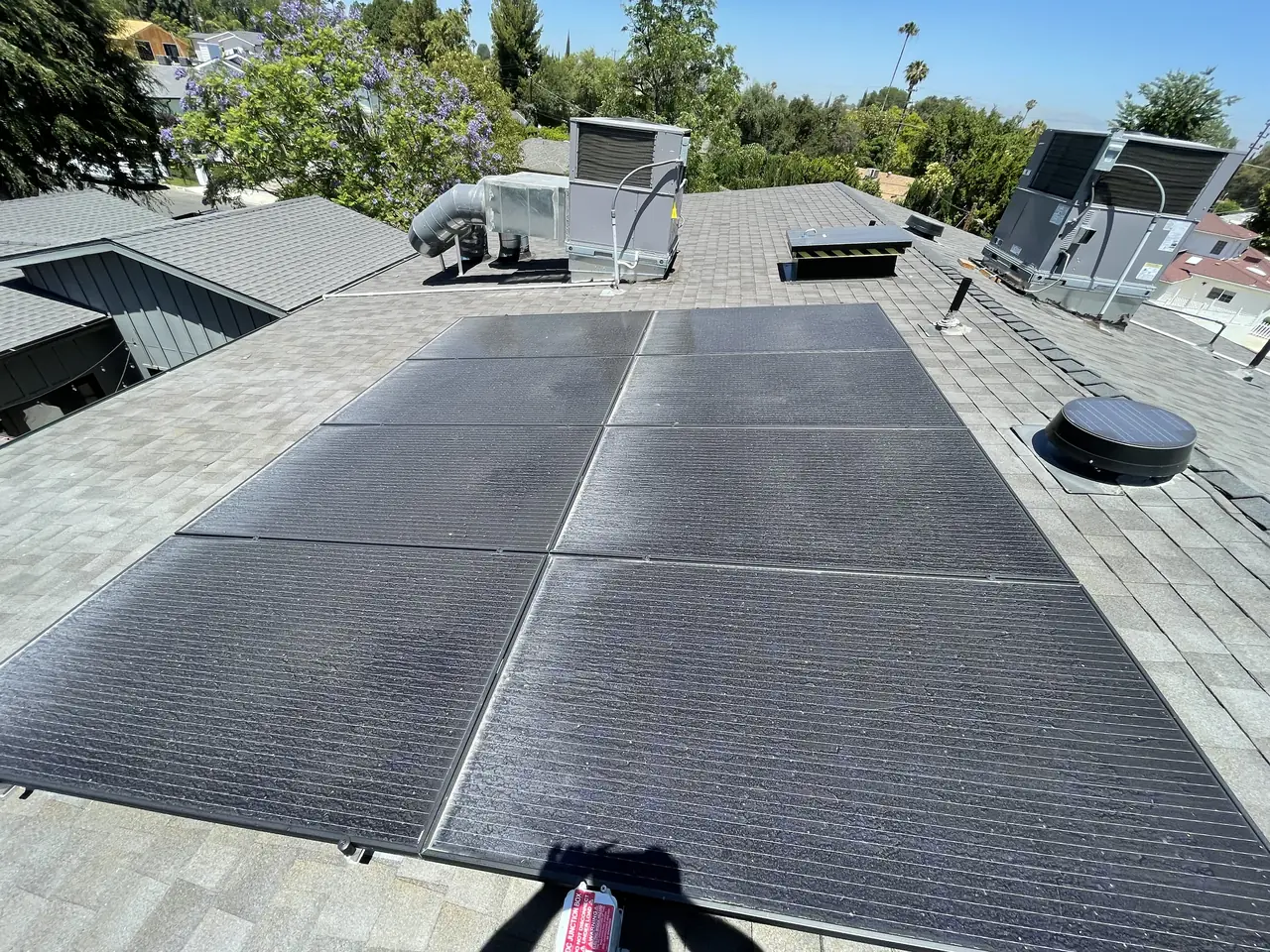 Solar modules on the composition shingle roof of a new house, with rooftop mechanical units beyond, Encino