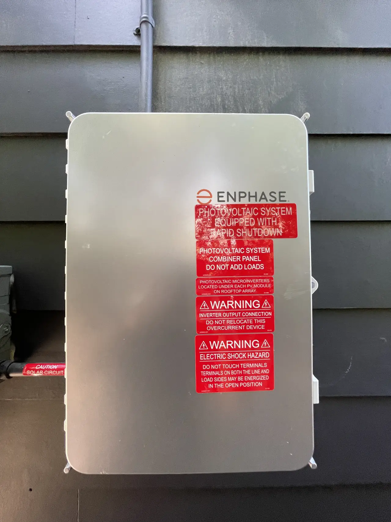 Enphase combiner panel with rapid shutdown and photovoltaic warning labels mounted on the siding of a new house