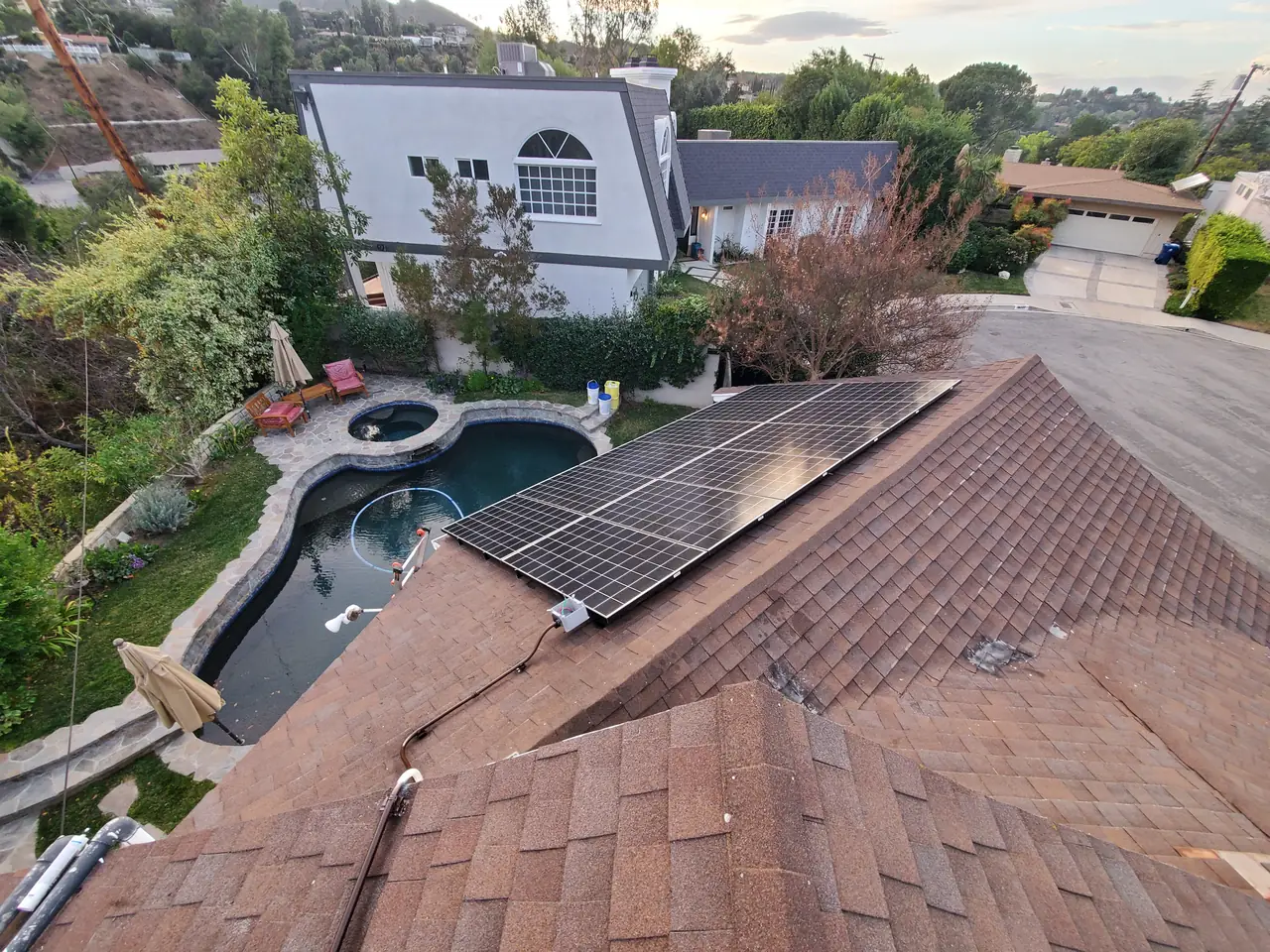 Solar modules on a hip roof above a pool in Encino, with neighboring houses on the hillside beyond