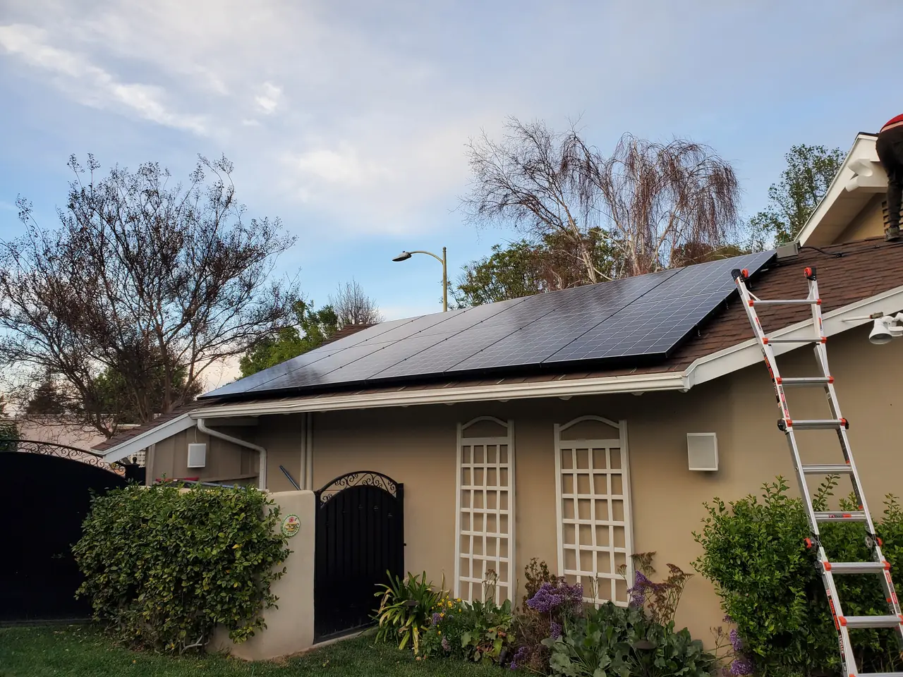 Single-story house from the street with solar modules on the roof and a ladder against the wall, Encino