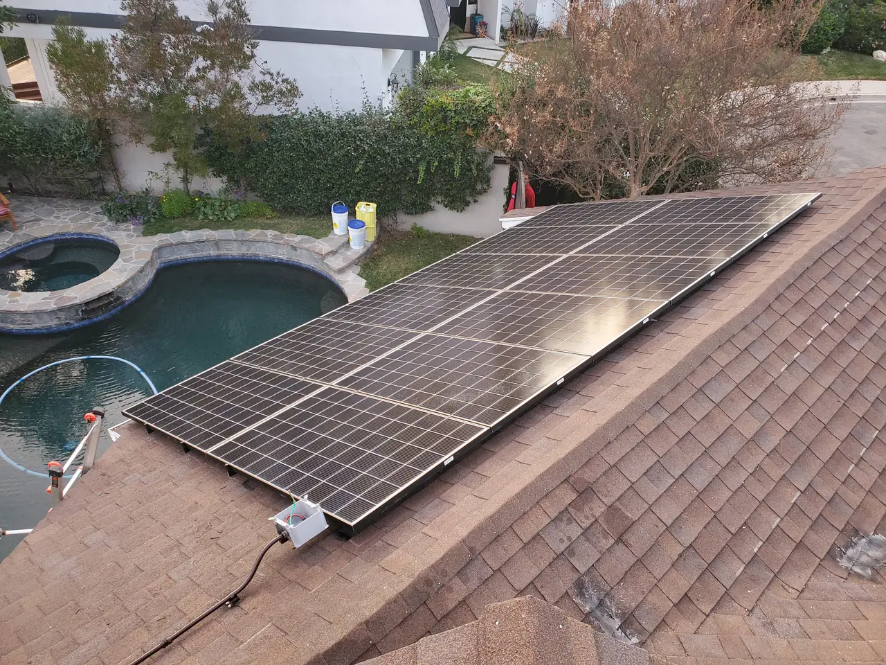 Solar modules running down a shingle slope above a pool, with a junction box at the array edge, Encino