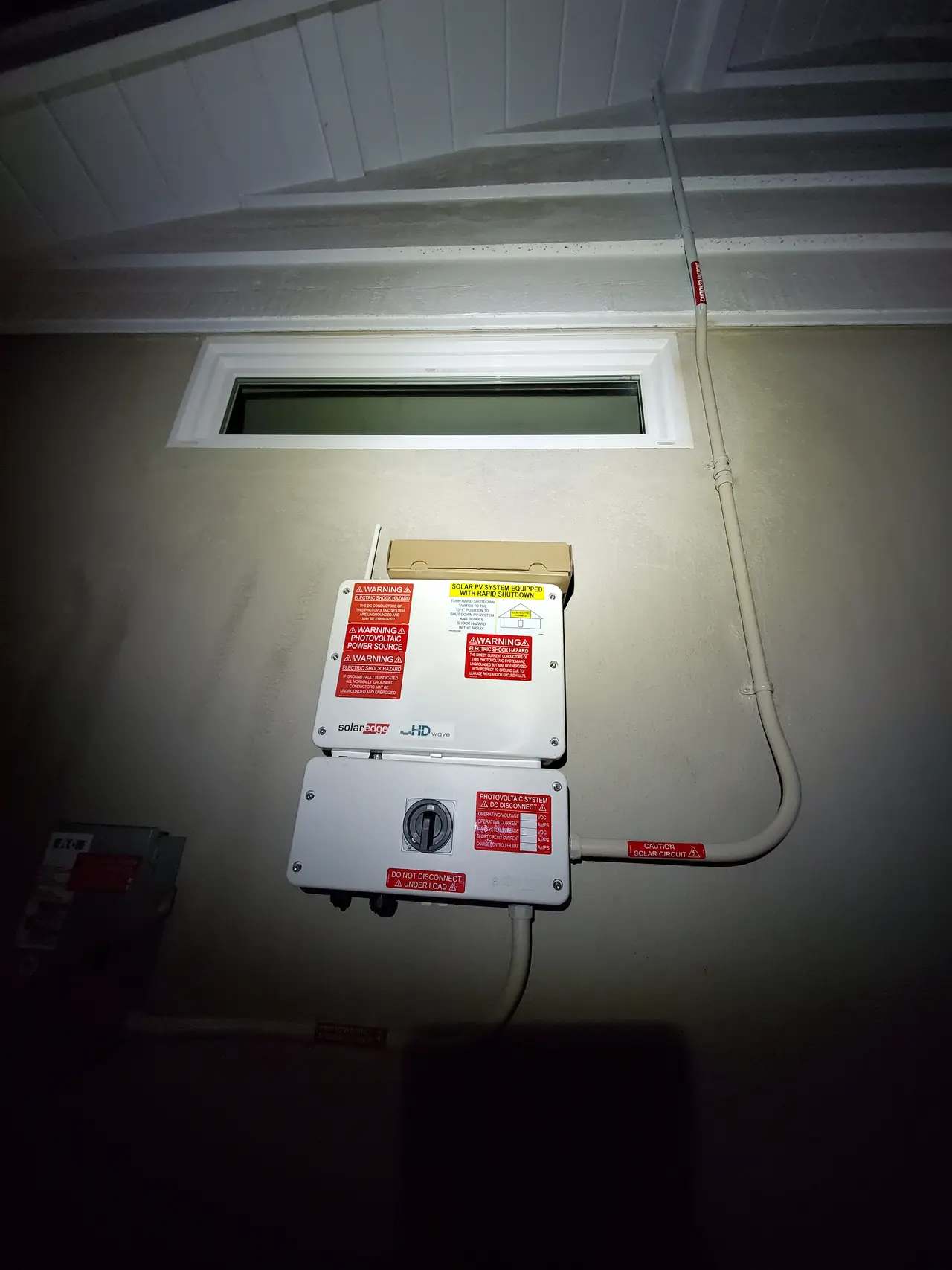SolarEdge string inverter and disconnect mounted on a garage wall beside the service equipment