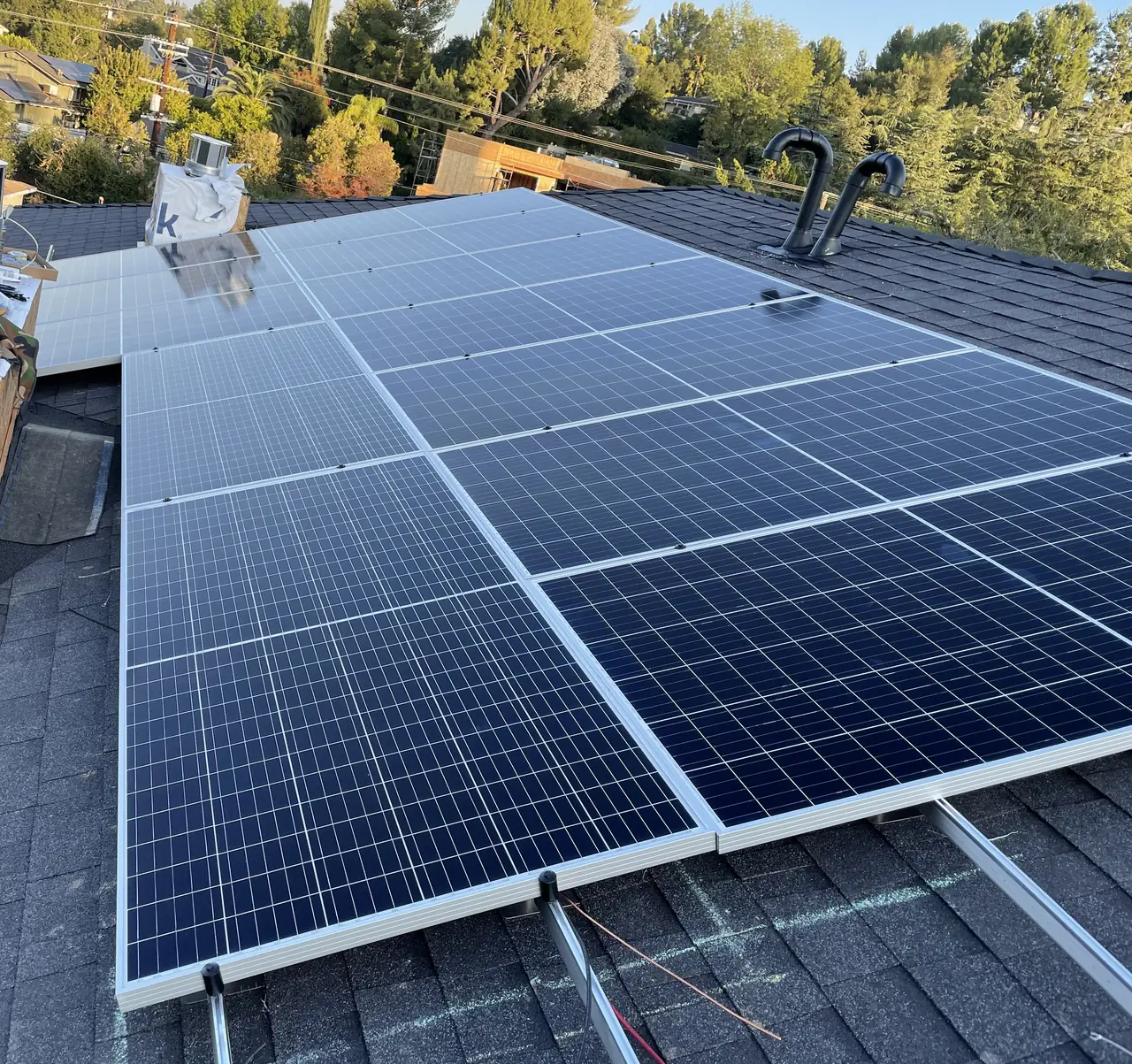Solar modules on a composition shingle roof at golden hour with a hillside neighborhood beyond, Encino