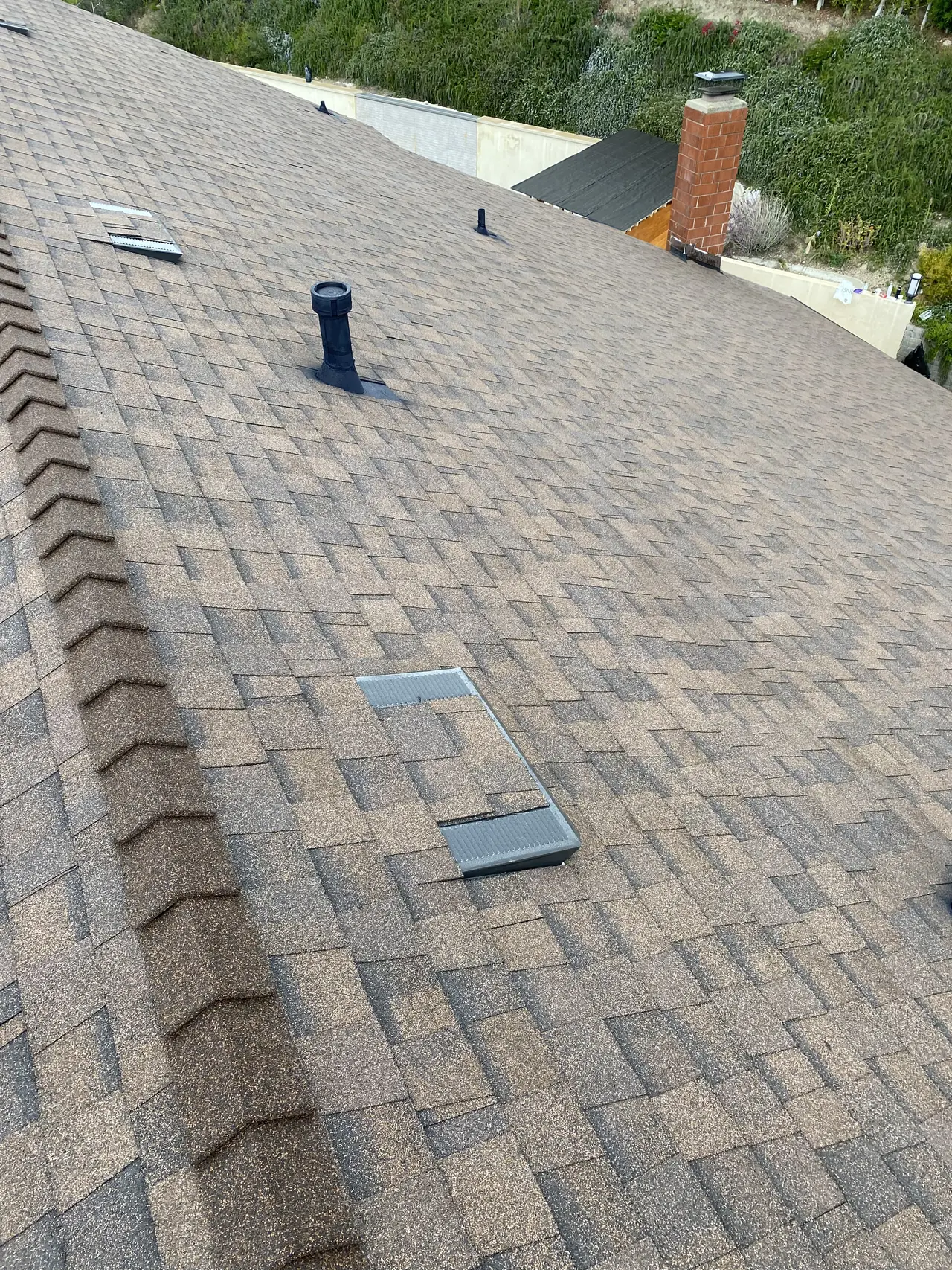 New composition shingle running up to a brick chimney, with trees on the slope beyond, Glendale