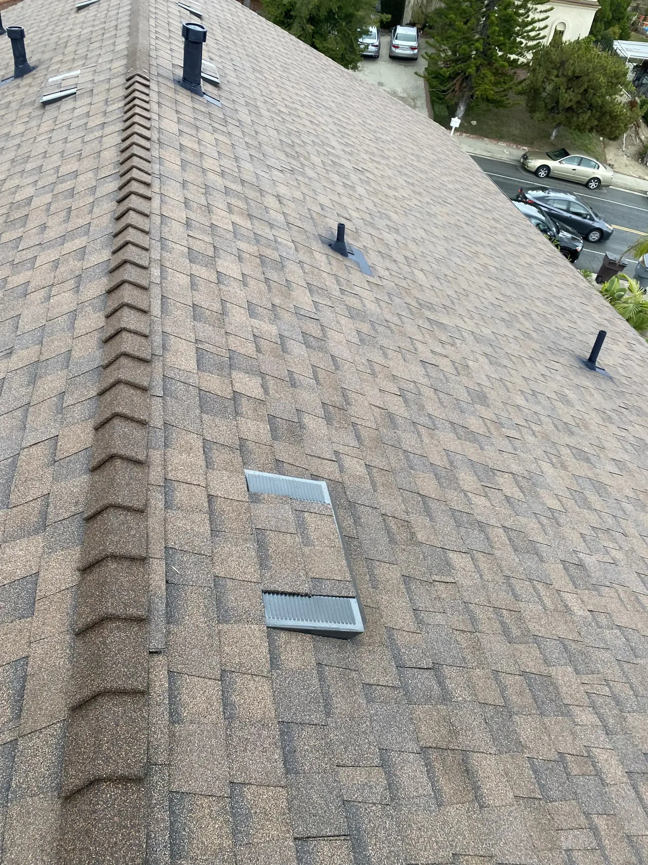 New composition shingle along a roof ridge with vents, looking down toward a residential street, Glendale