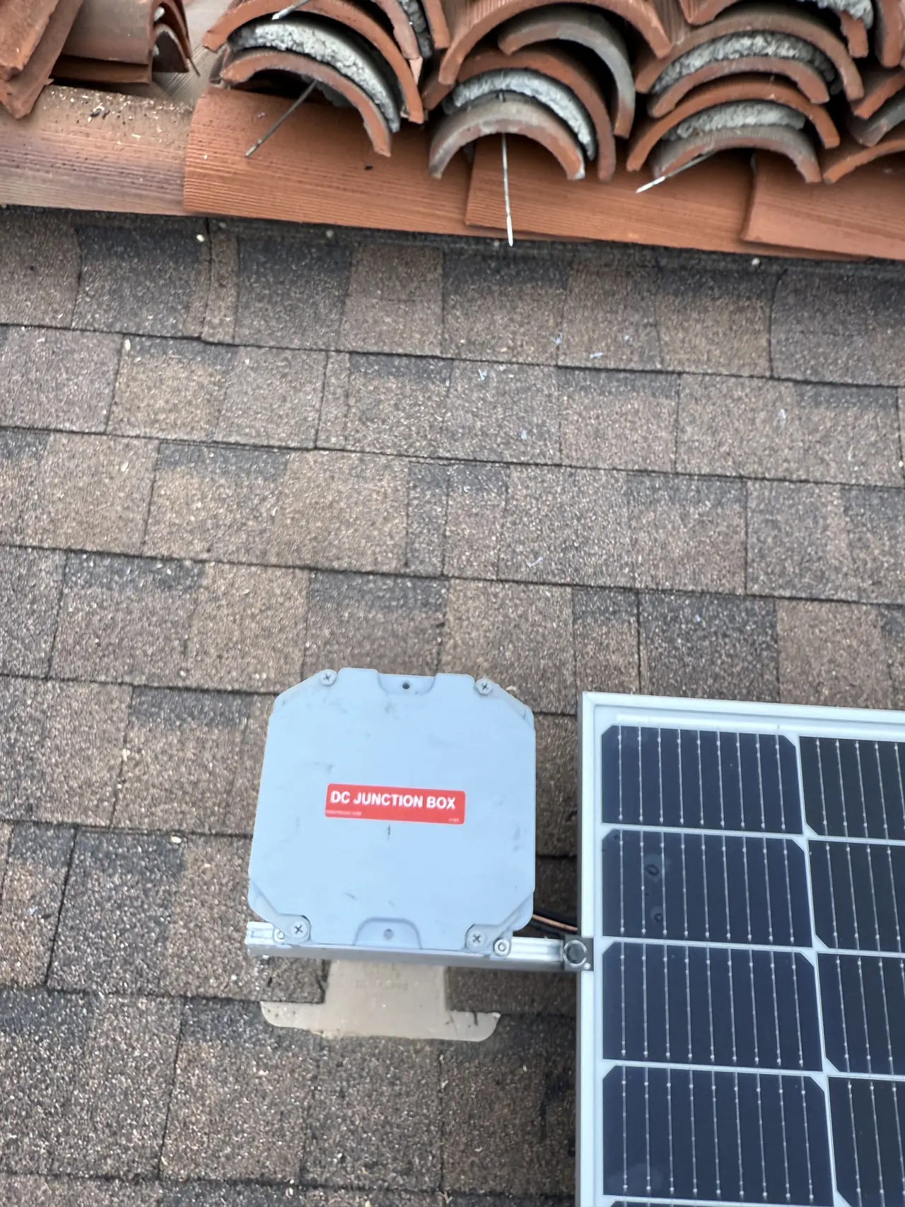 Composition shingle meeting a row of clay barrel tile at a roof ridge, with a junction box and a module edge, Glendale