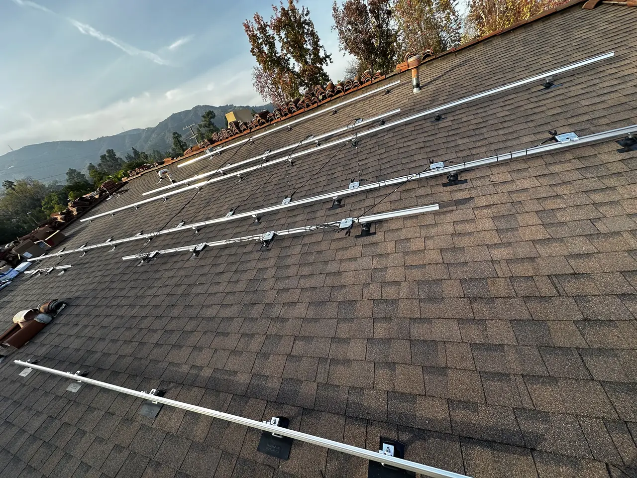 Aluminum mounting rails on flashed feet across a new composition shingle field, with clay tile at the edges and mountains beyond, Glendale