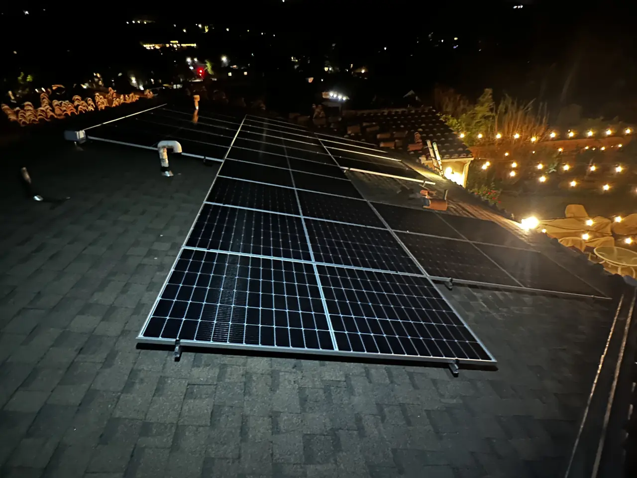 Solar array on a shingle roof at night, lit by string lights in the neighboring yard, Glendale