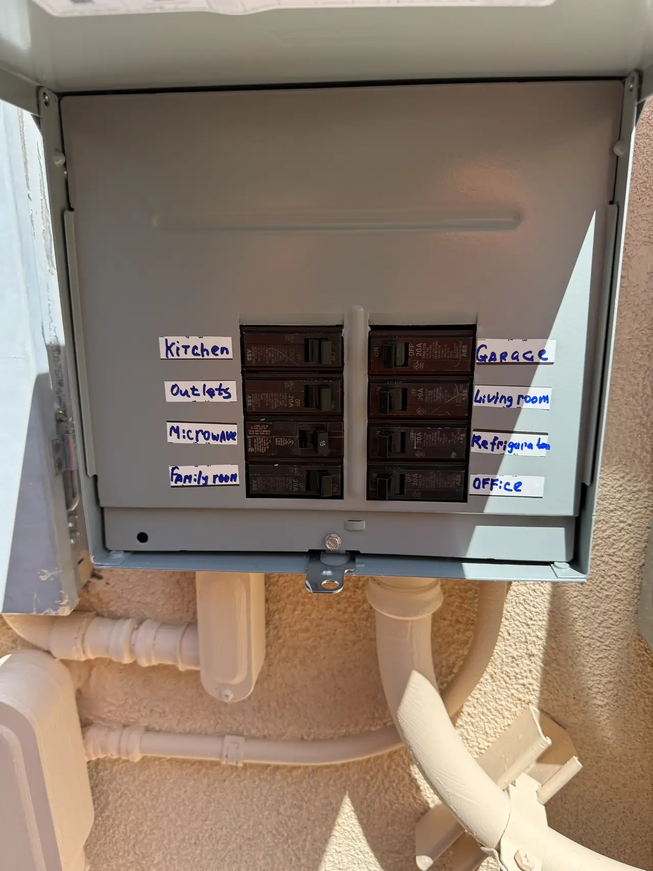 Open backup load panel with handwritten labels on the breakers for kitchen outlets, microwave, refrigerator, family room, living room, office and garage, Glendale