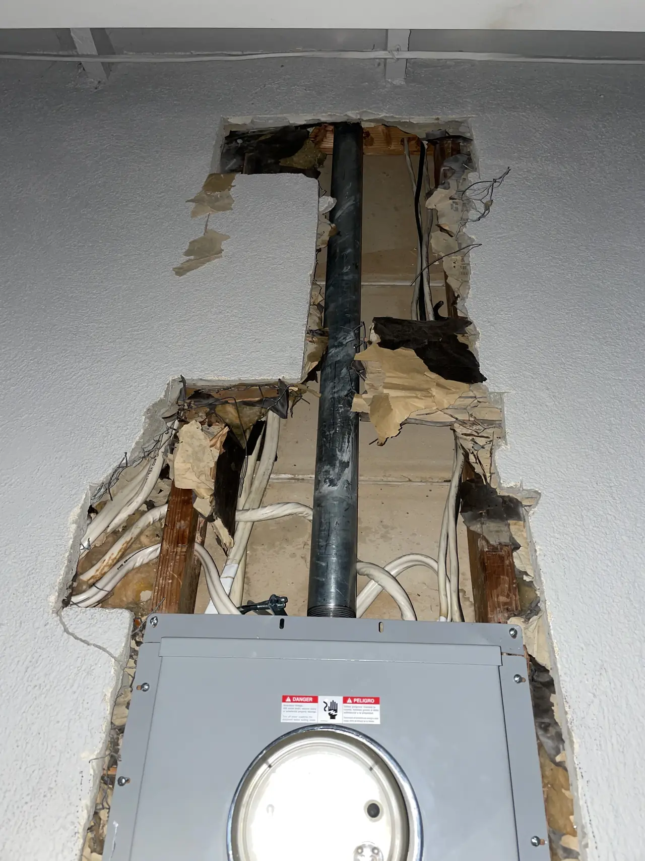 Stucco wall cut open above a new electrical panel to run the service conduit, with the old wiring exposed, Glendale