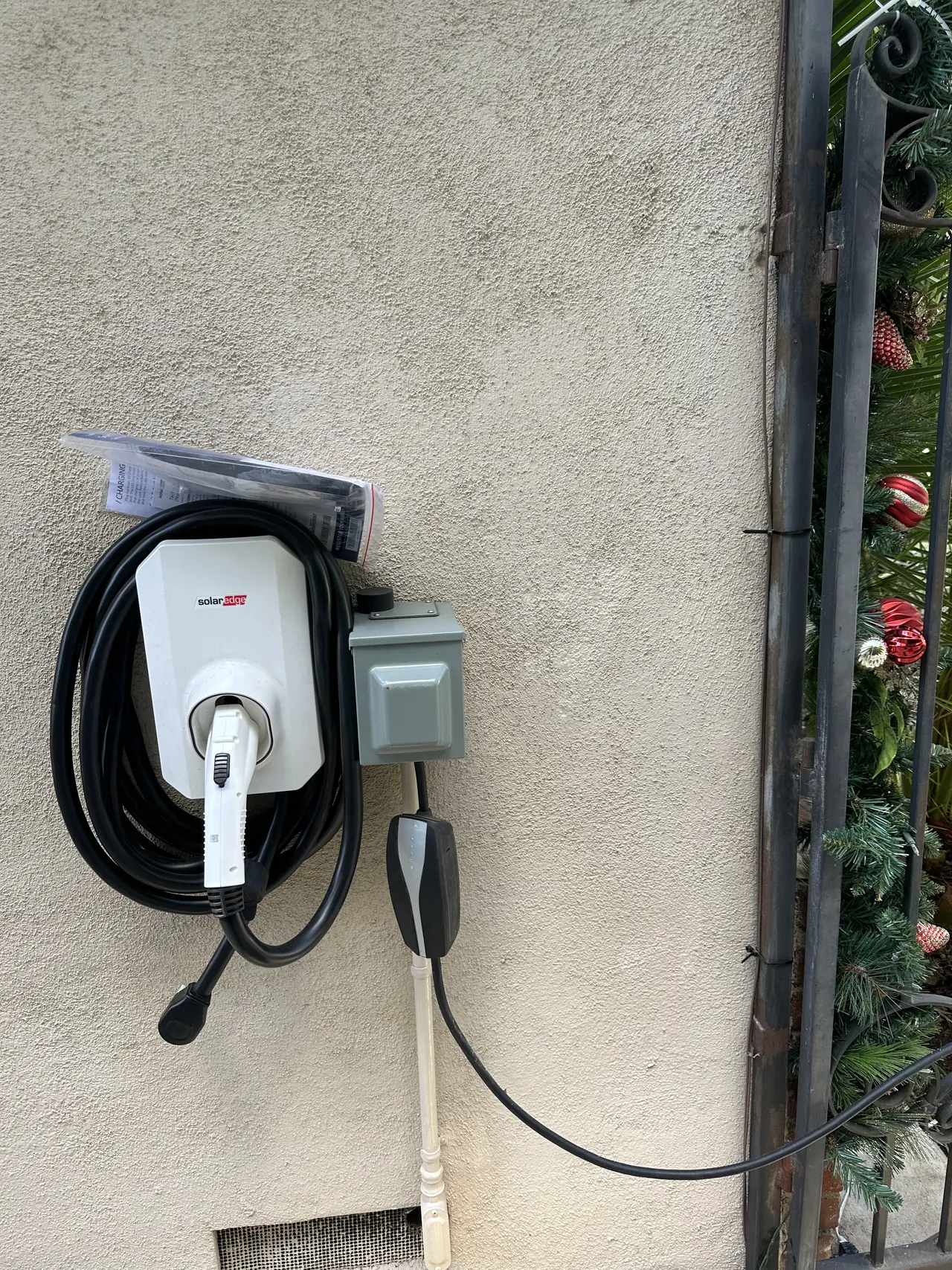 Wall-mounted electric-vehicle charger with its cable coiled, beside a small junction box on a stucco wall, Glendale