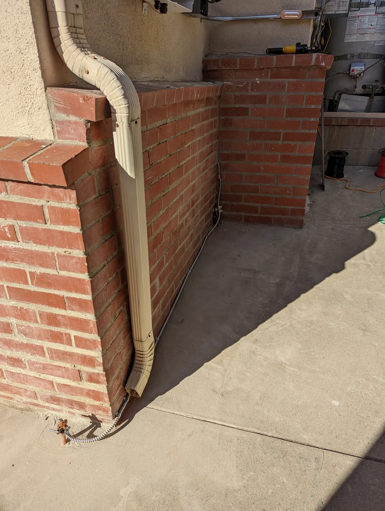 Conduit emerging from concrete at the base of a brick planter and rising up a stucco wall, Glendale