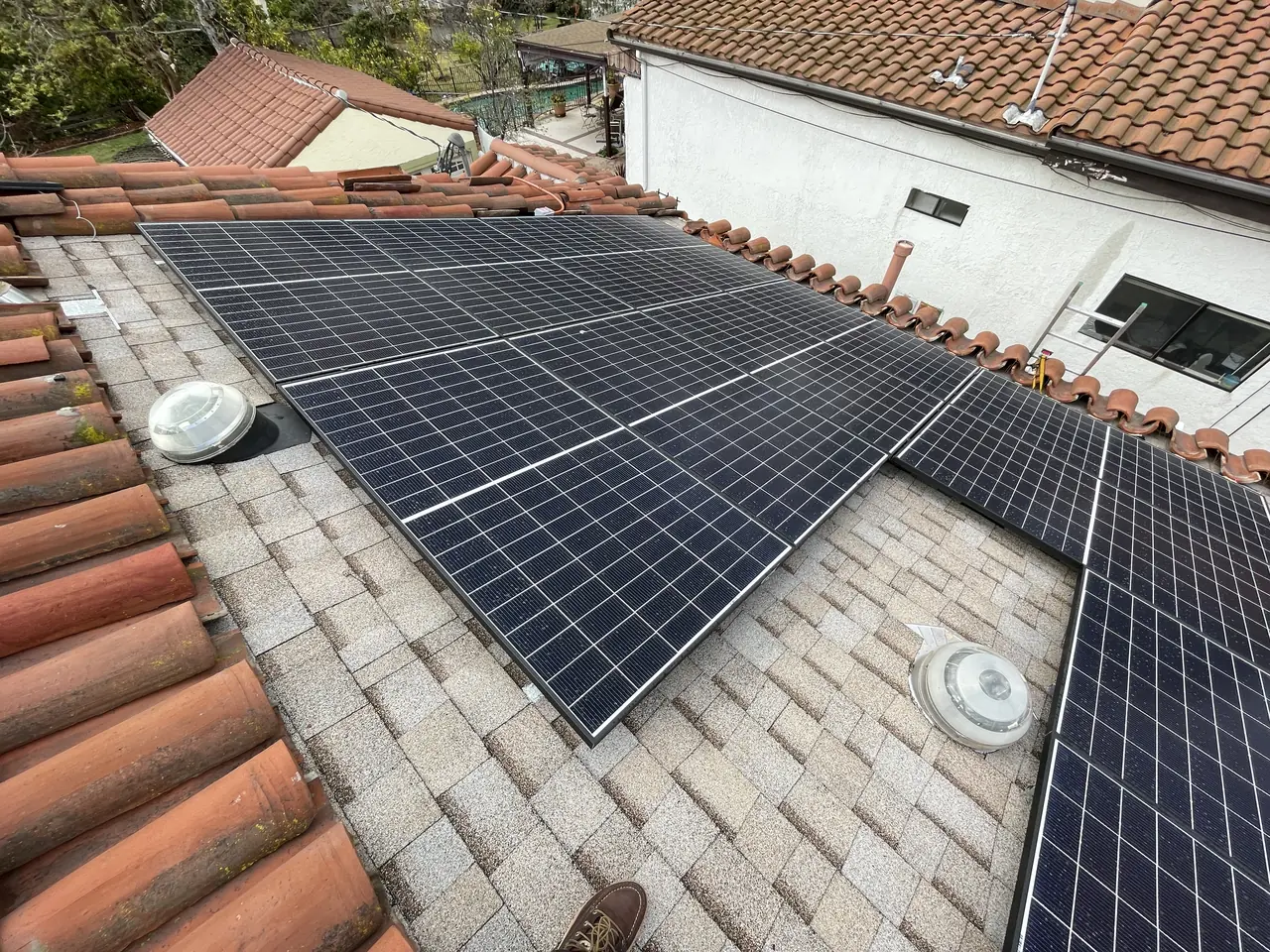 Modules on a shingle field beside a ridge of clay barrel tile, with a second tiled roof and a stucco house behind, Glendale
