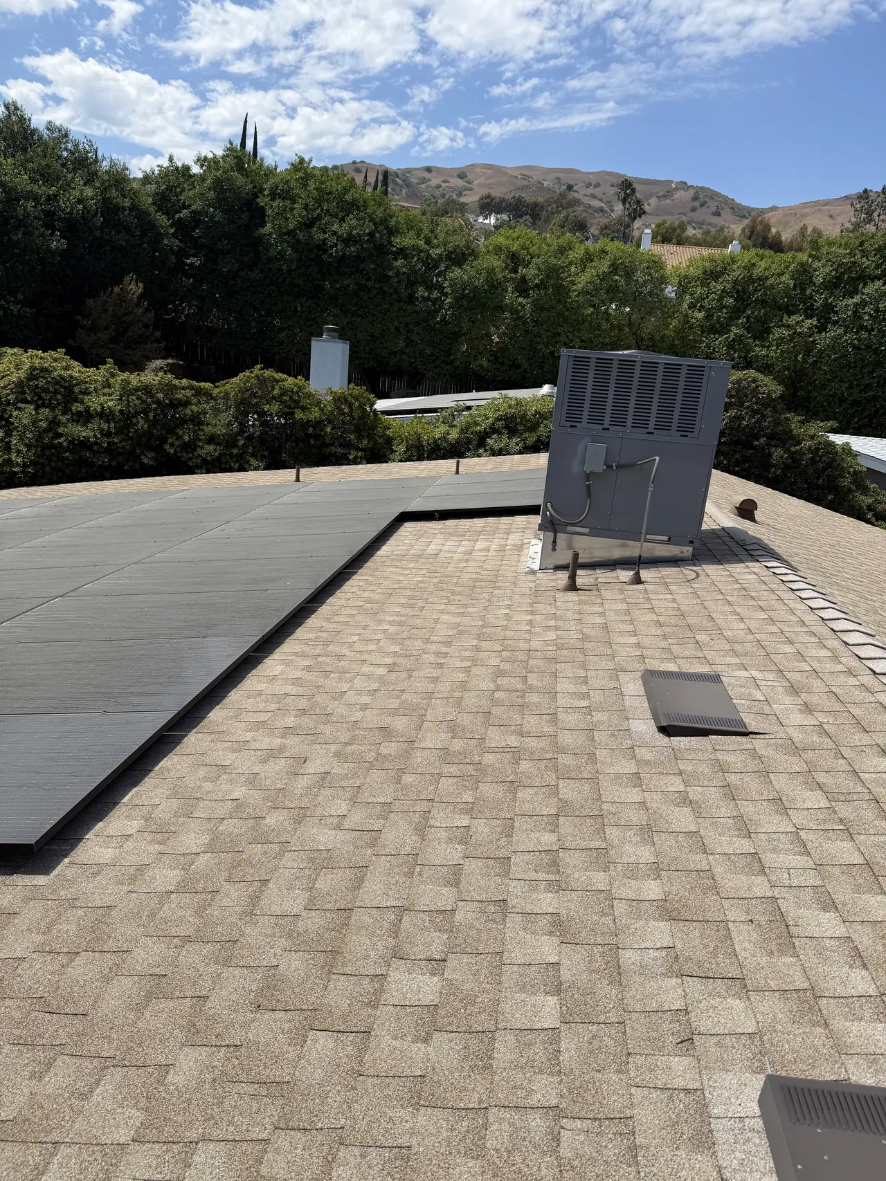 Solar array on a composition shingle roof beside a rooftop cooler, hills behind, Granada Hills