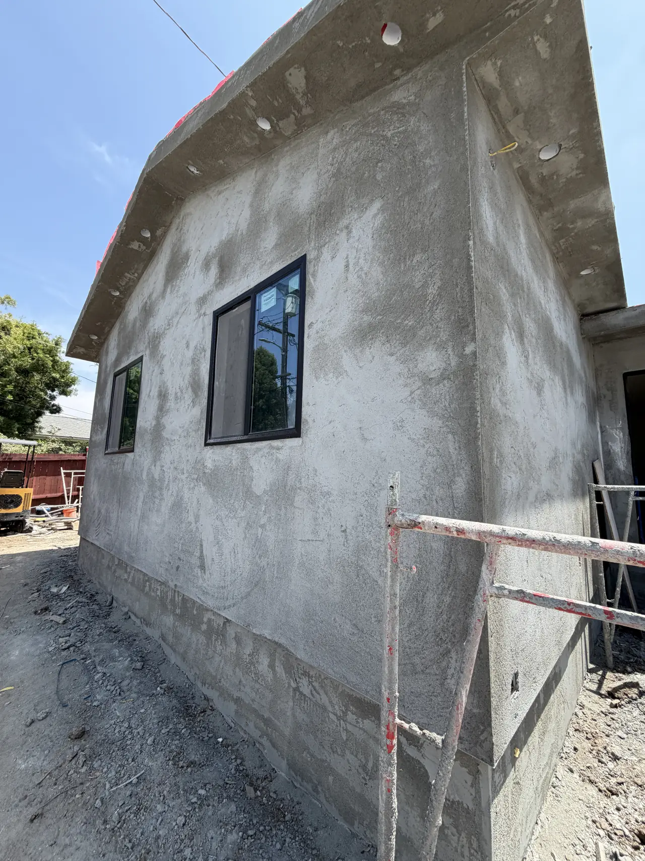 The end wall of a newly built unit in bare stucco with a window and scaffolding, Granada Hills