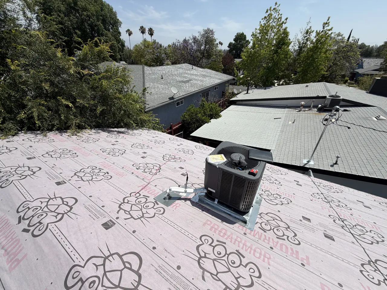 A flat roof covered in underlayment with a rooftop air-conditioning condenser and neighboring roofs beyond, Granada Hills
