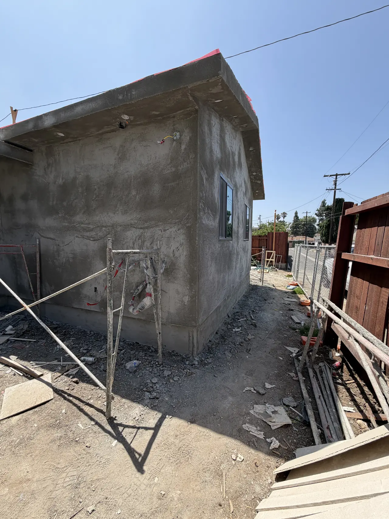The side of a newly built unit in bare stucco with scaffolding and a boundary fence, Granada Hills