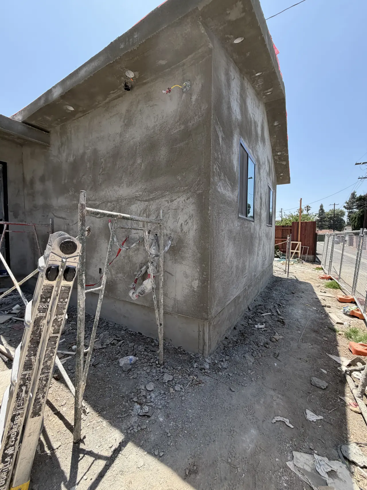 A newly built unit in bare stucco with a portable toilet and construction debris in the side yard, Granada Hills