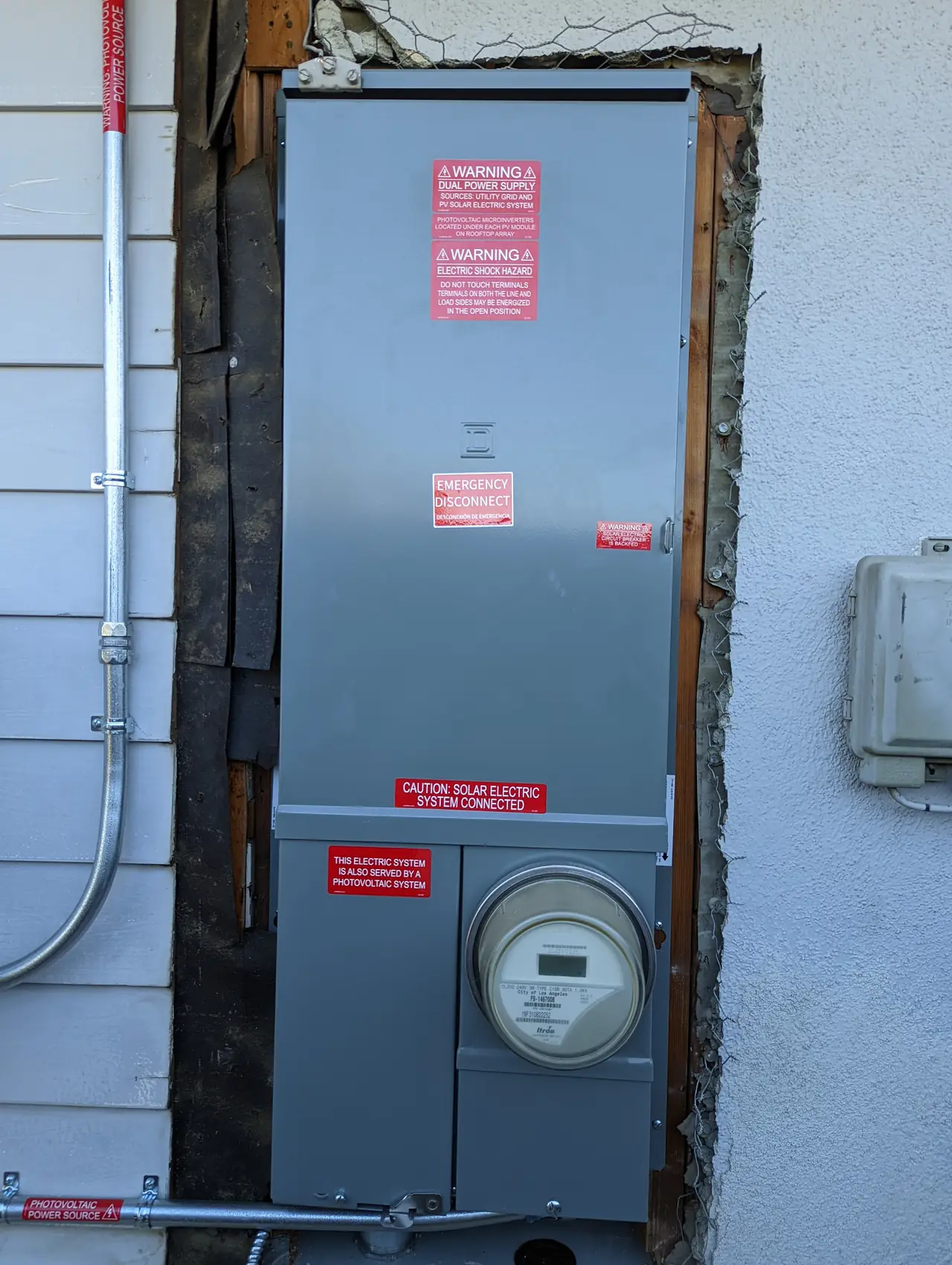 A new service panel and meter fitted into an opening cut in the wall, with bare framing and sheathing exposed around the edges, Granada Hills