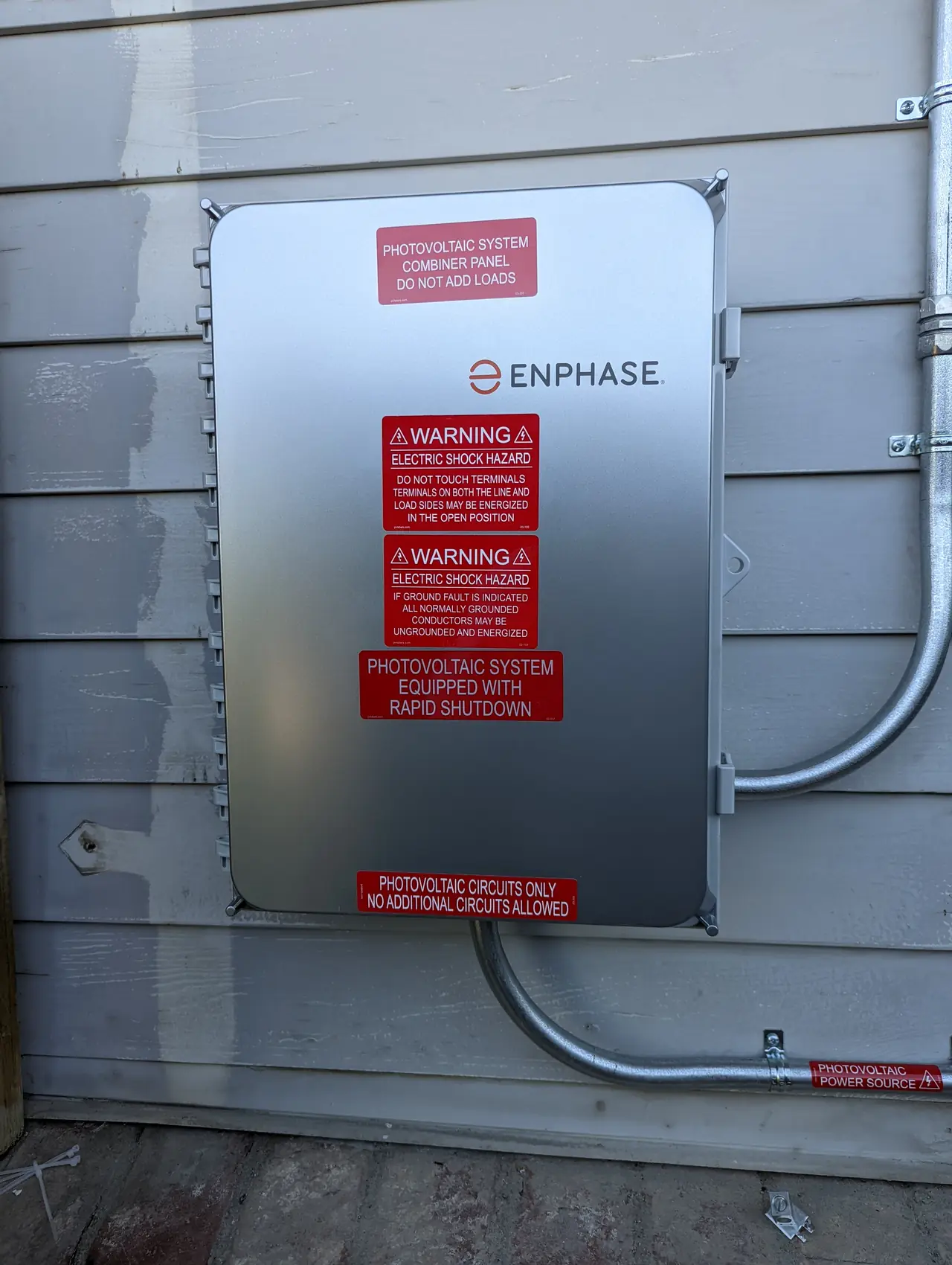 A combiner enclosure with warning placards closed on an exterior wall, Granada Hills