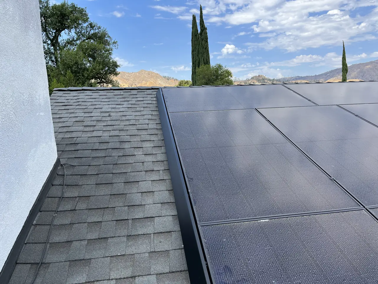 A dark solar array running up a composition shingle roof with trees and hills beyond, Granada Hills