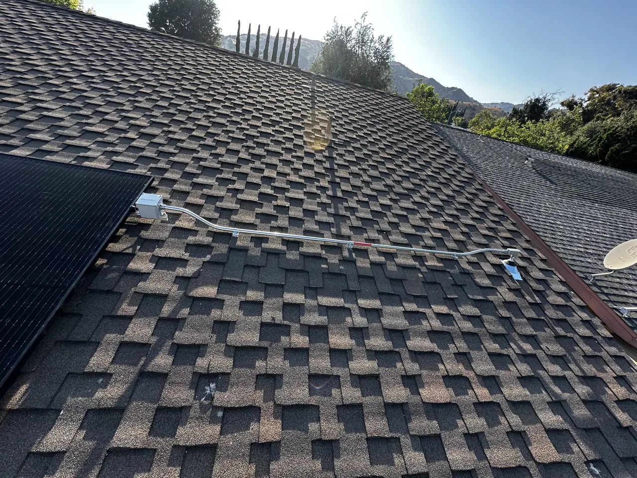 A dark solar array across two planes of a composition shingle roof with hills beyond, Granada Hills