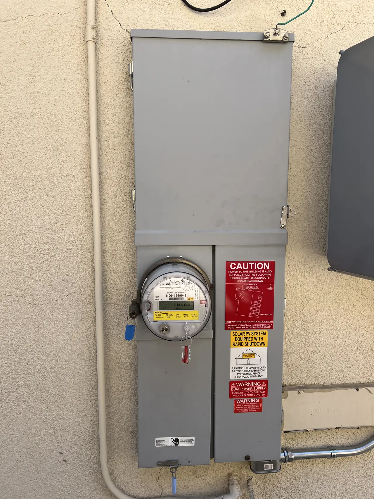 A meter and service panel on a stucco wall with solar warning placards, Granada Hills