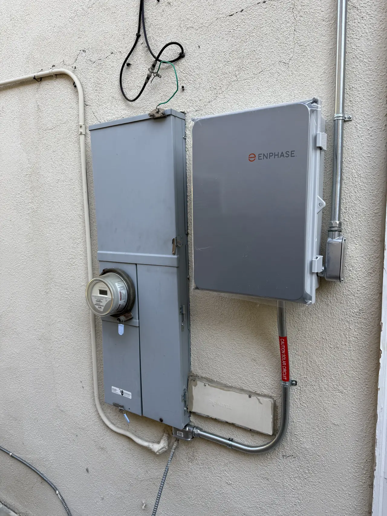 A combiner enclosure and meter mounted on an exterior stucco wall, closed and labeled, Granada Hills